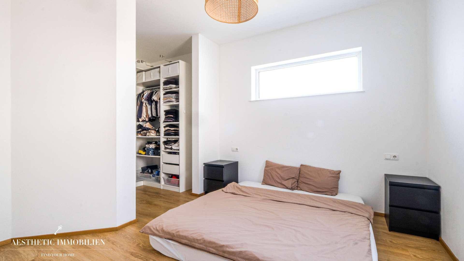 Schlafzimmer mit Holzboden, Doppelbett und offenem Kleiderschrankbereich.