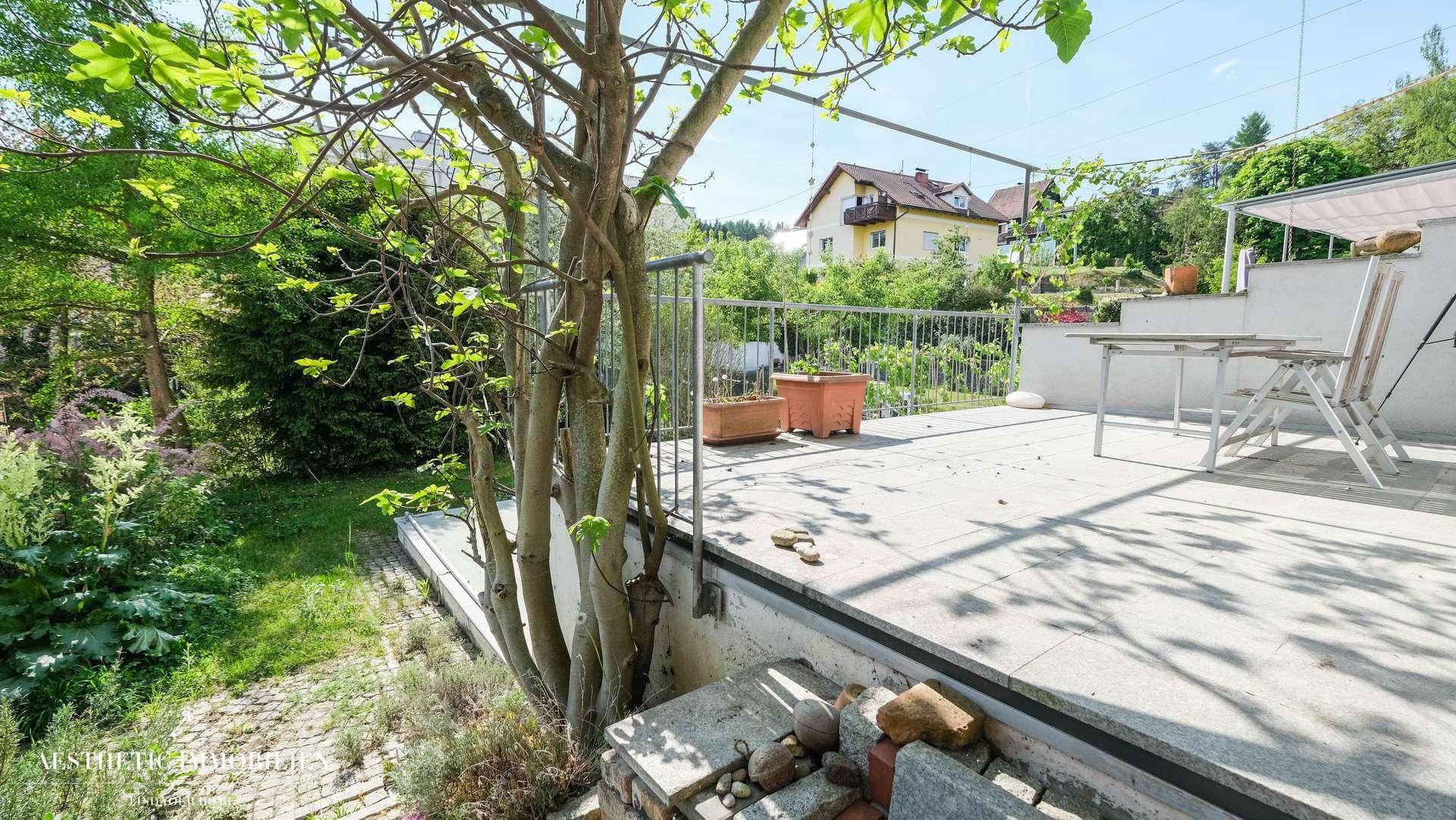 Geräumige Terrasse mit Sitzgelegenheiten und Treppenzugang zu einem grünen Gartenbereich.