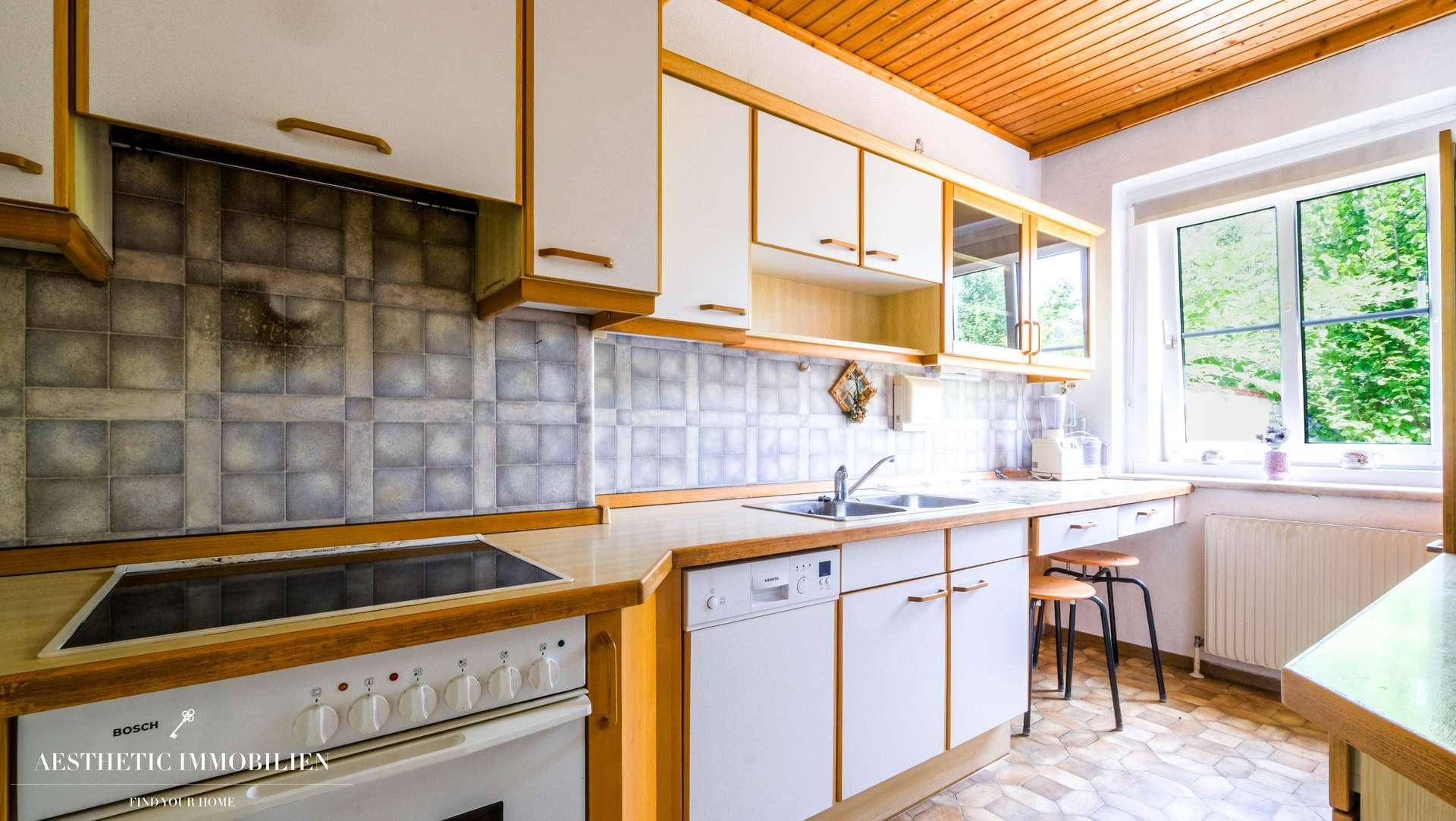 Funktionale Küche mit Holzdecke, Einbaugeräten und Fenster mit Blick ins Grüne.