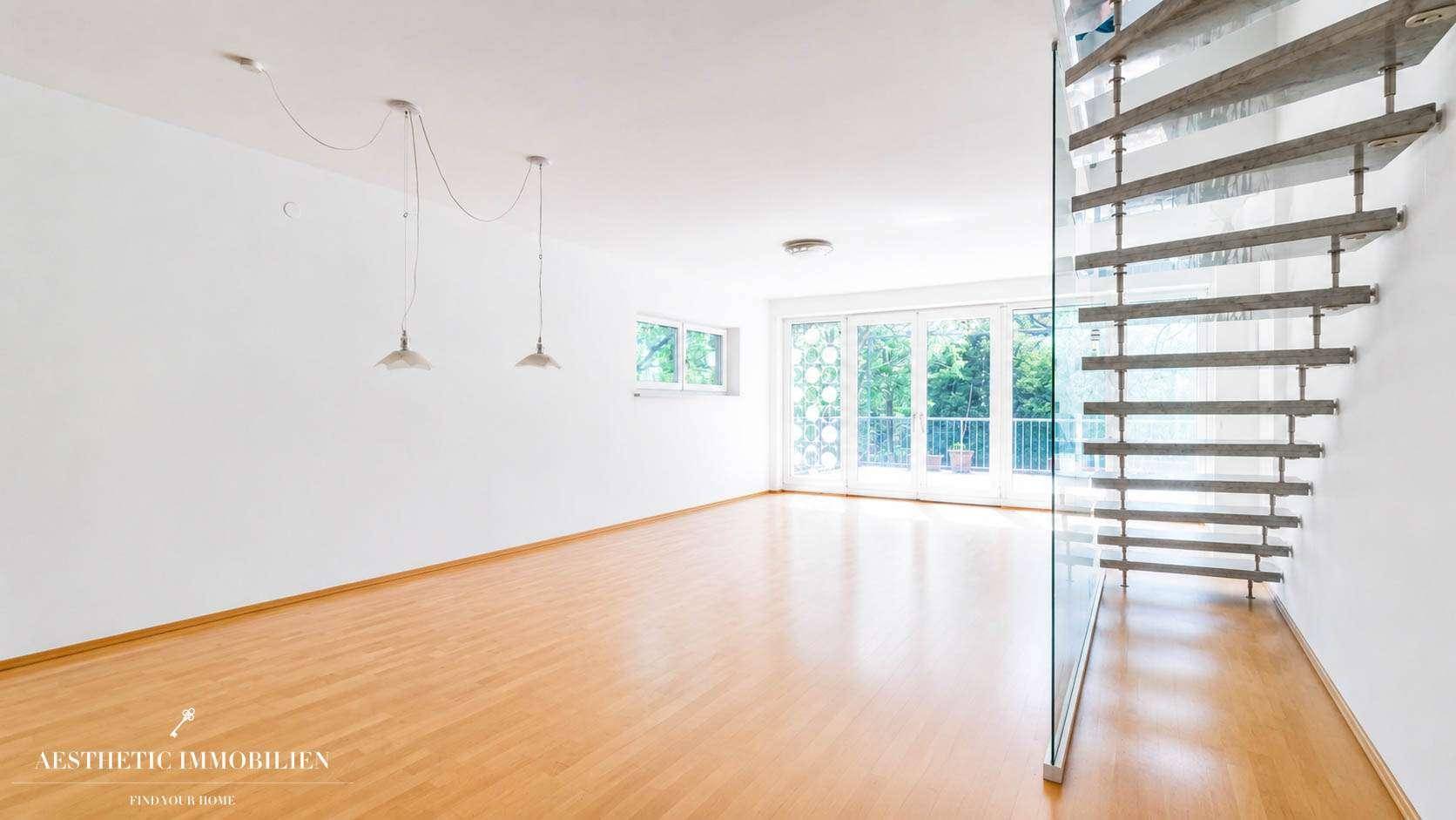Geräumiges, leeres Wohnzimmer mit hellem Holzboden, großen Fenstern und moderner Glastreppe.