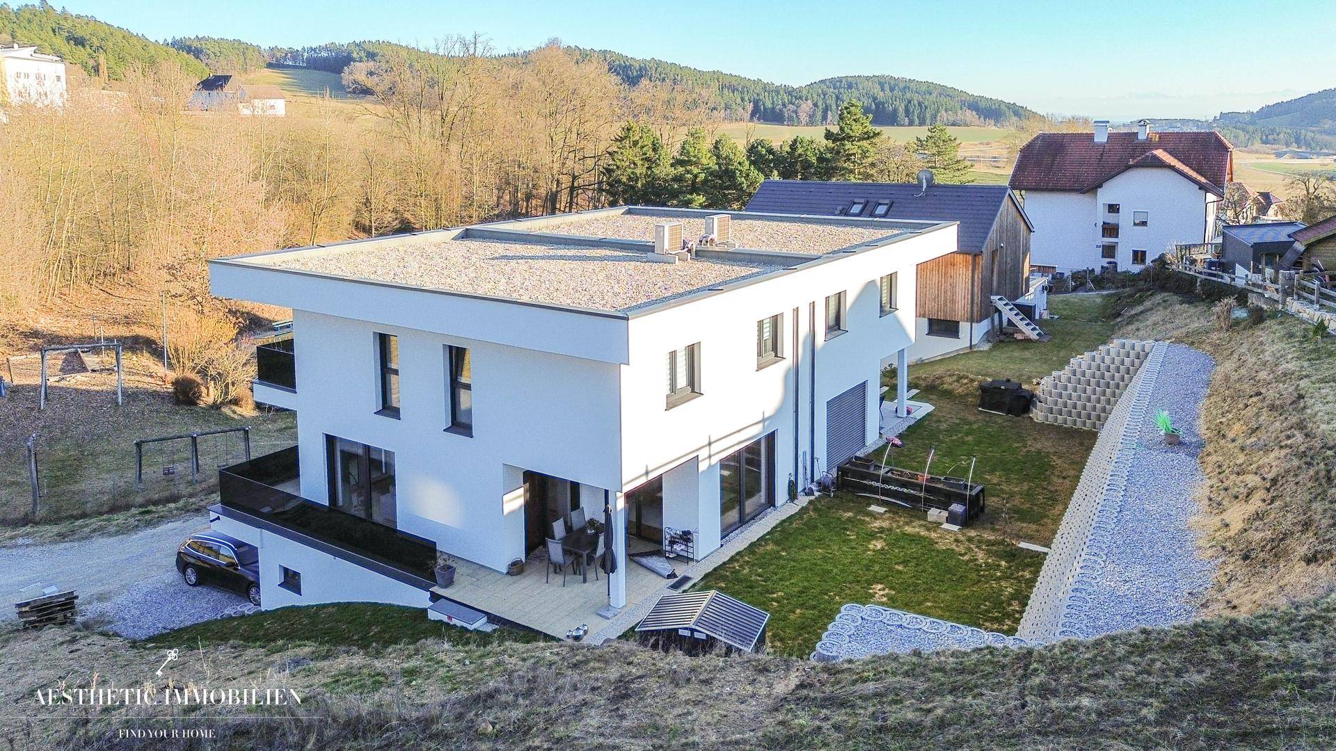 Vogelperspektive eines modernen Hauses mit Flachdach, Garten und umliegender Natur.