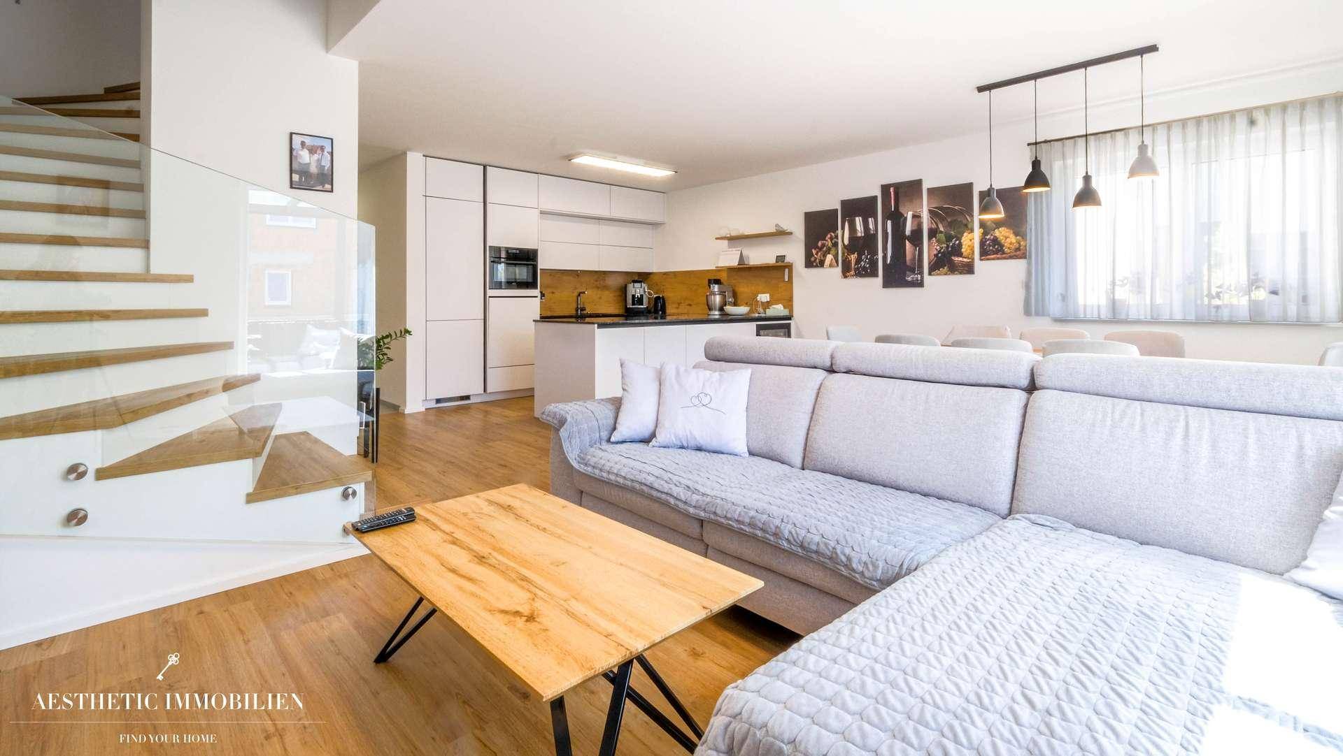 Gemütliches Wohnzimmer mit Ecksofa, Holztisch und offener Treppe zum Obergeschoss.