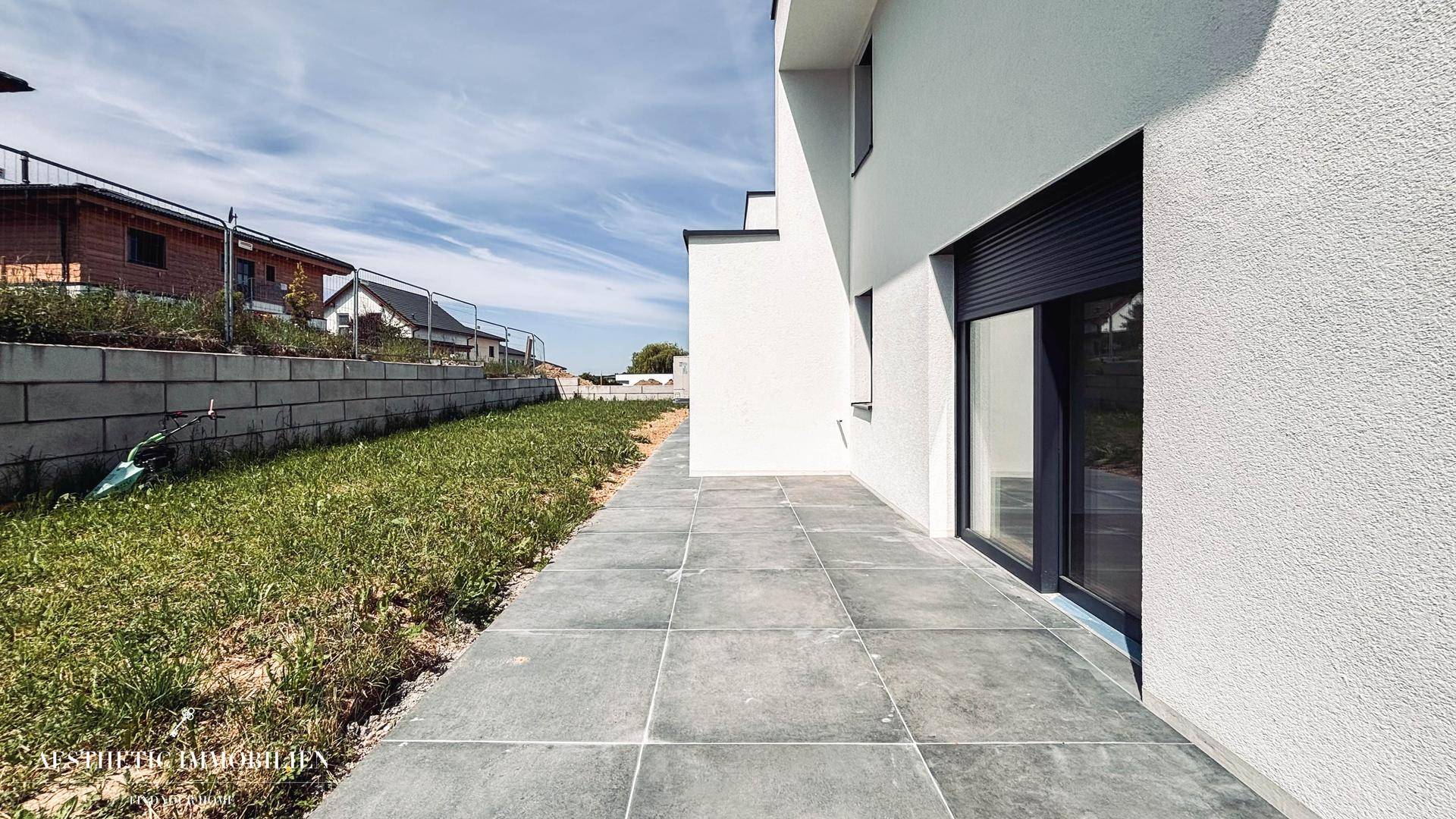 Gepflasterte Terrasse entlang der Hausseite mit Zugang zu den Innenräumen.
