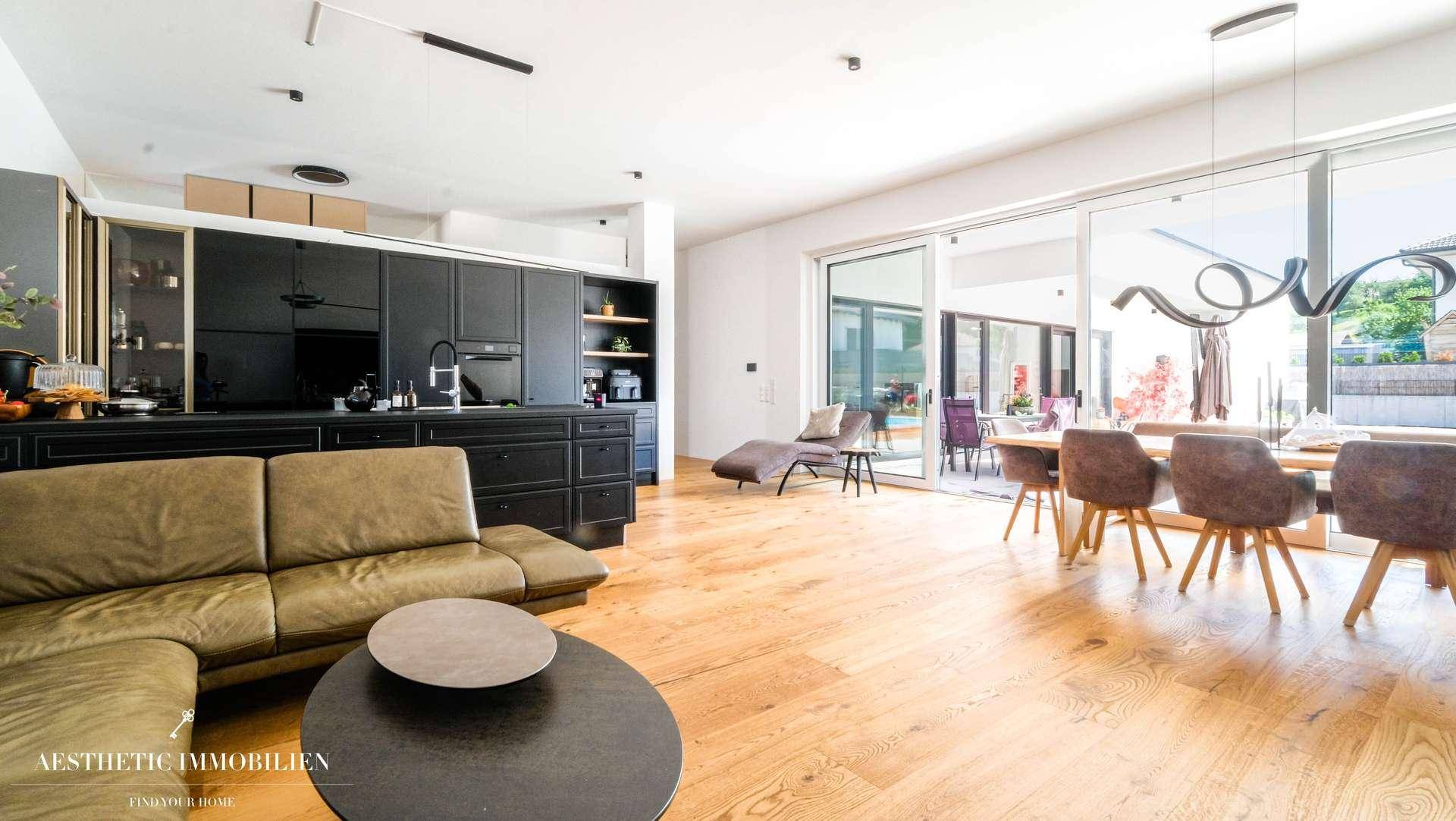 Heller offener Wohn-Essbereich mit moderner Küche, Holzboden und Zugang zur Terrasse.