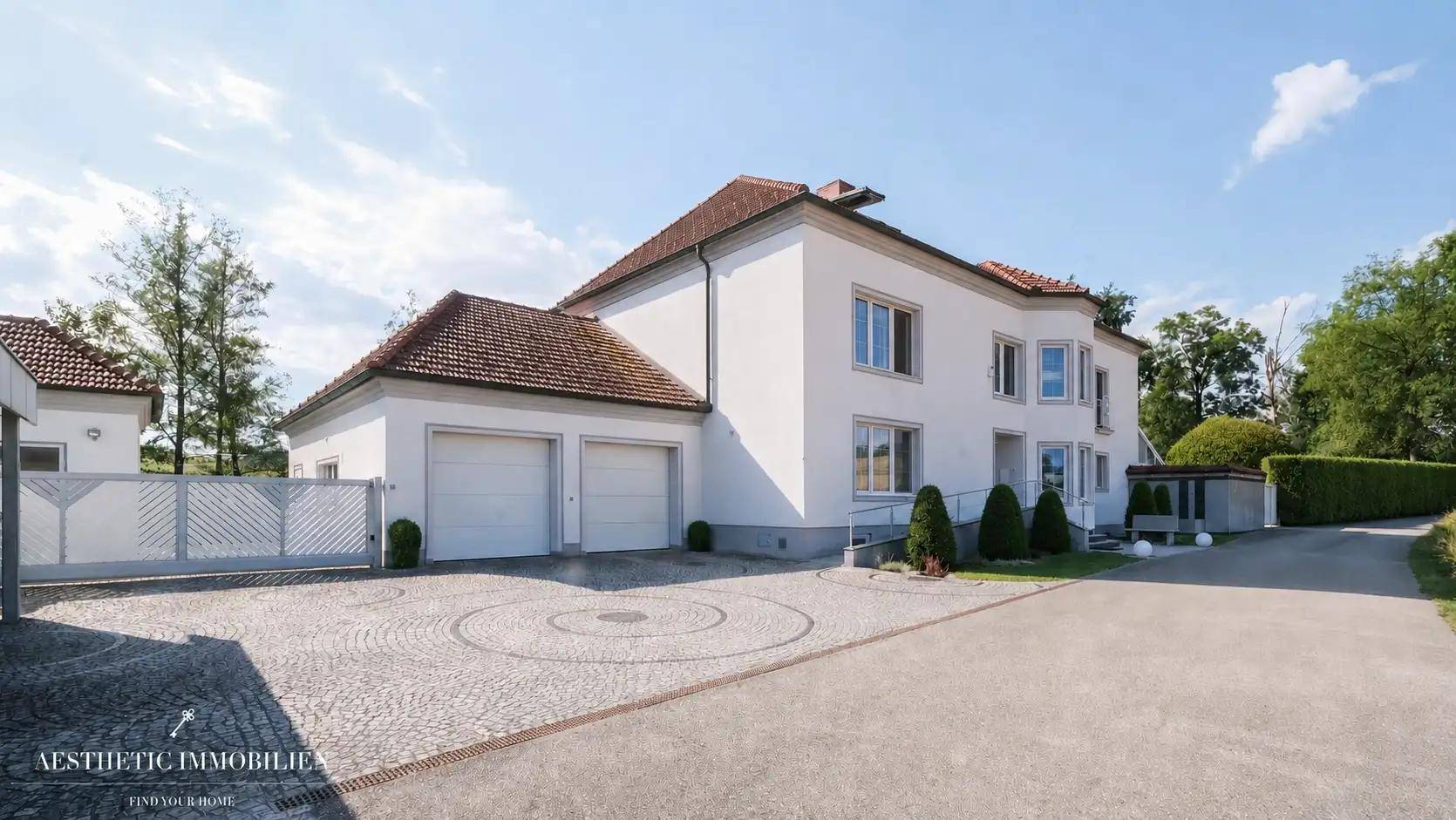 Ansicht des Hauses mit Doppelgarage, gepflastertem Hof und breiter Zufahrt.