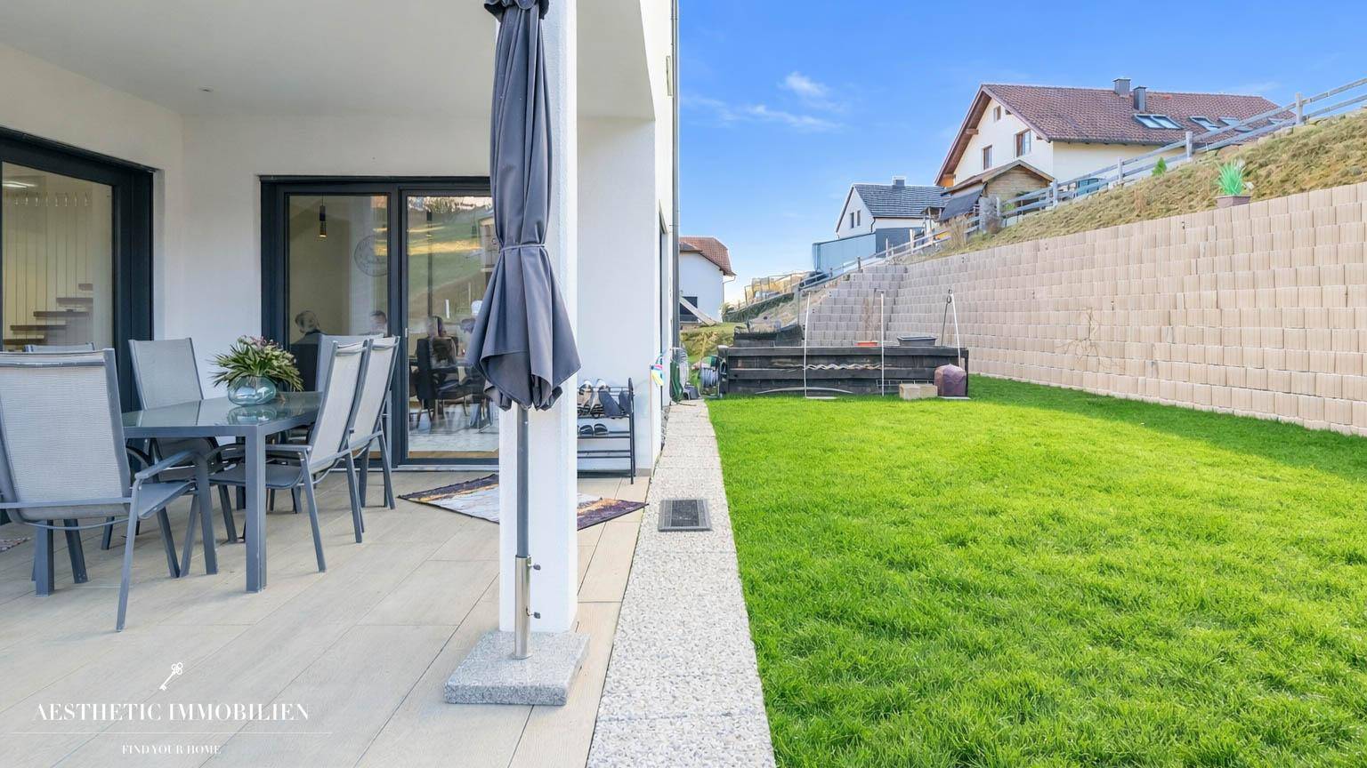 Sonniger Terrassenbereich mit Gartenmöbeln und Blick auf den gepflegten Rasen und die Umgebung.