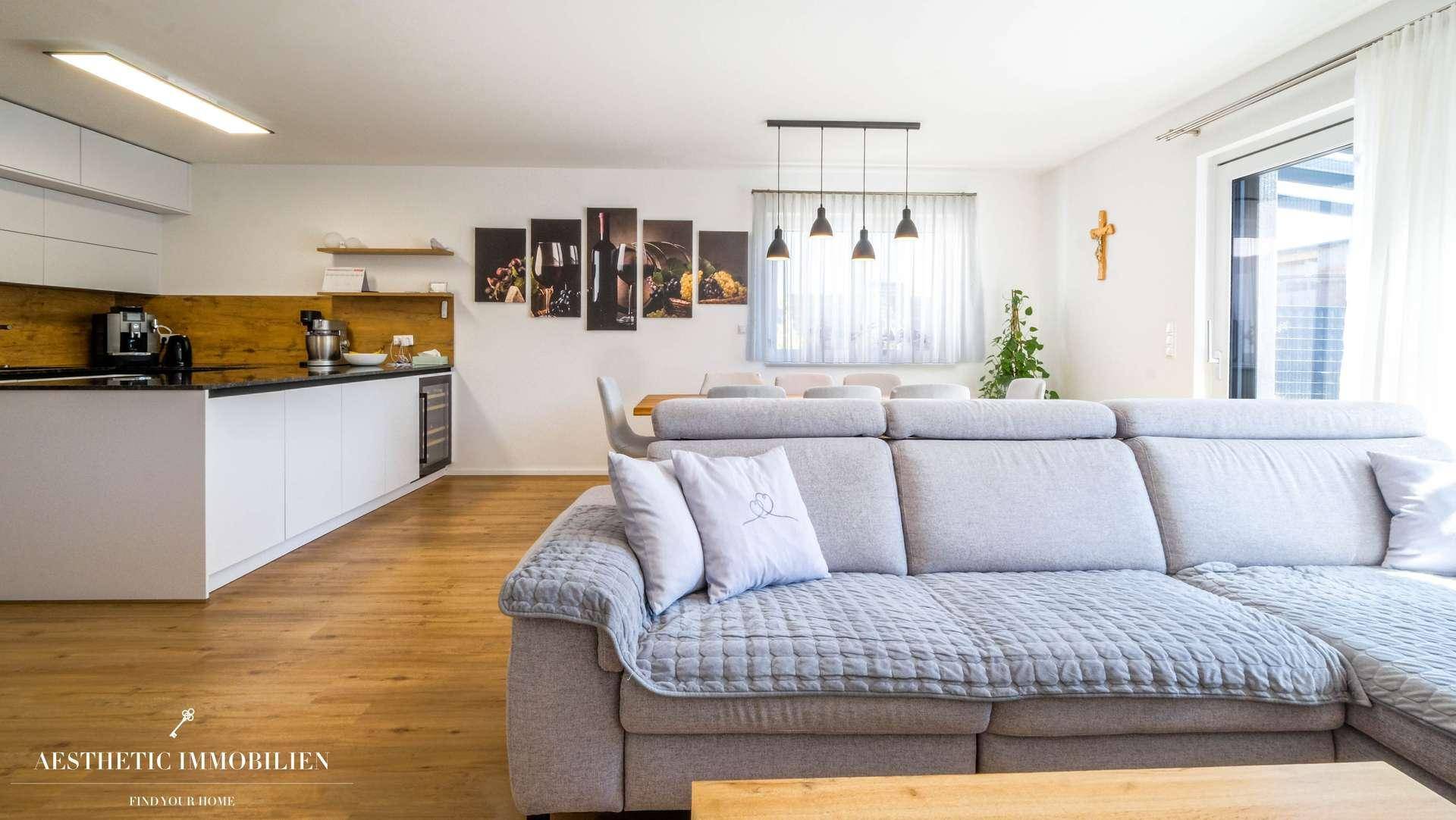 Heller Wohnbereich mit bequemer Couch, Essbereich und offener Küche im Hintergrund.