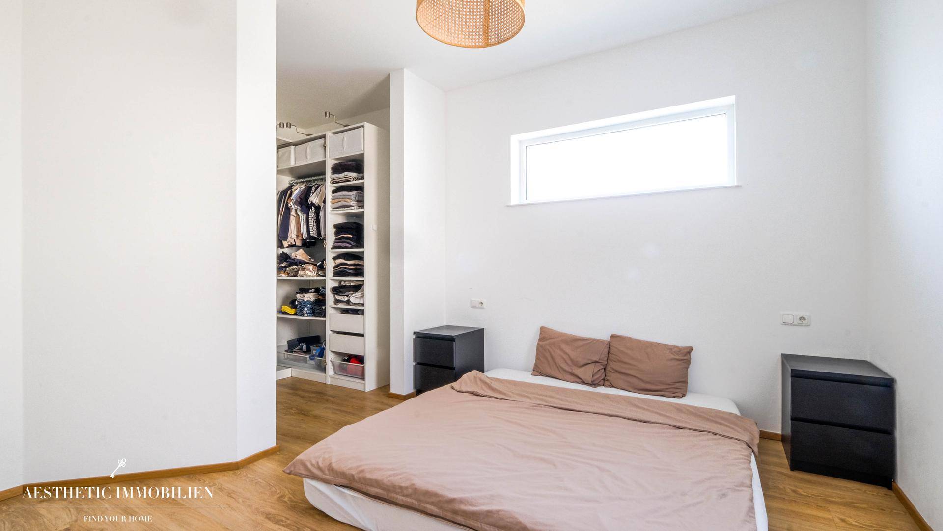 Schlafzimmer mit Doppelbett, schmalem Fenster und offenem begehbarem Kleiderschrank.