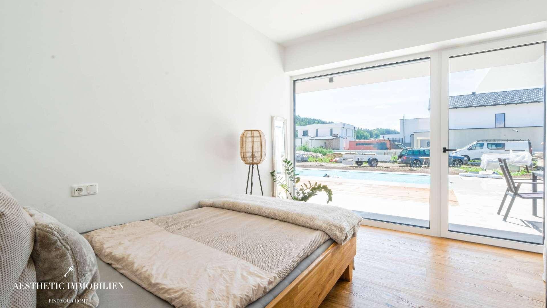 Gemütliches Schlafzimmer mit Holzboden und großen Fenstern mit Blick auf den Außenbereich.