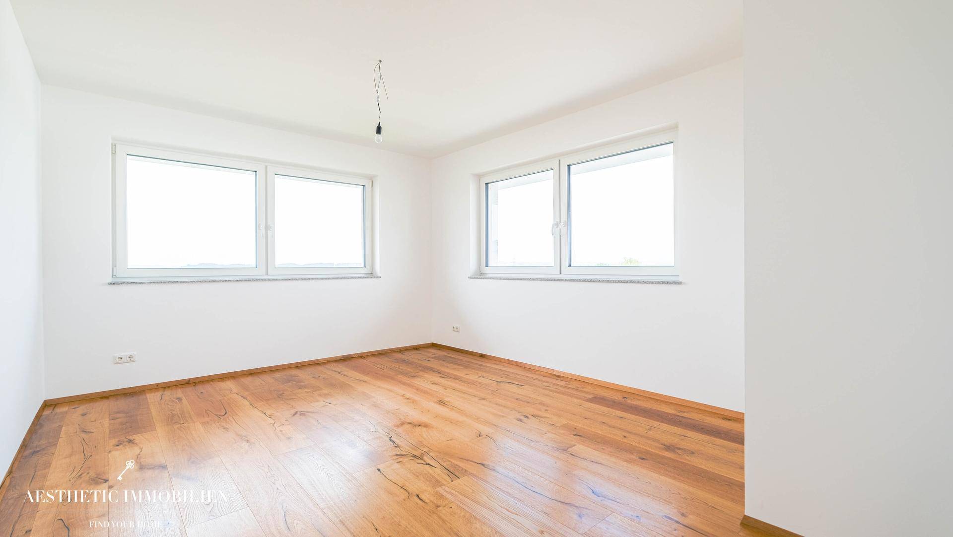 Heller, unmöblierter Raum mit Holzboden und zwei Fenstern, ideal als Schlaf- oder Arbeitszimmer.