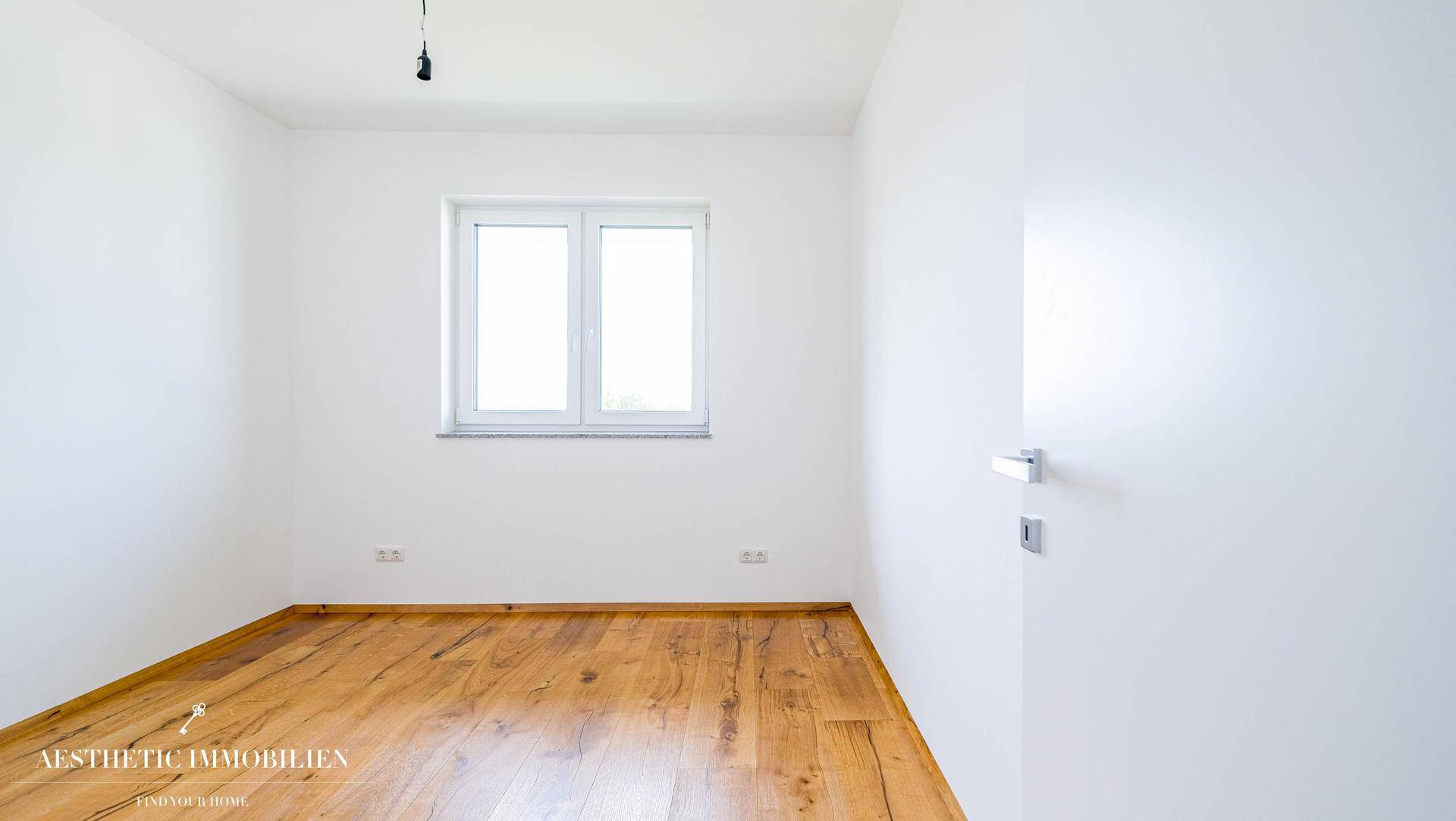 Kleiner, heller Raum mit Holzboden und einem Fenster, geeignet als Kinder- oder Gästezimmer.