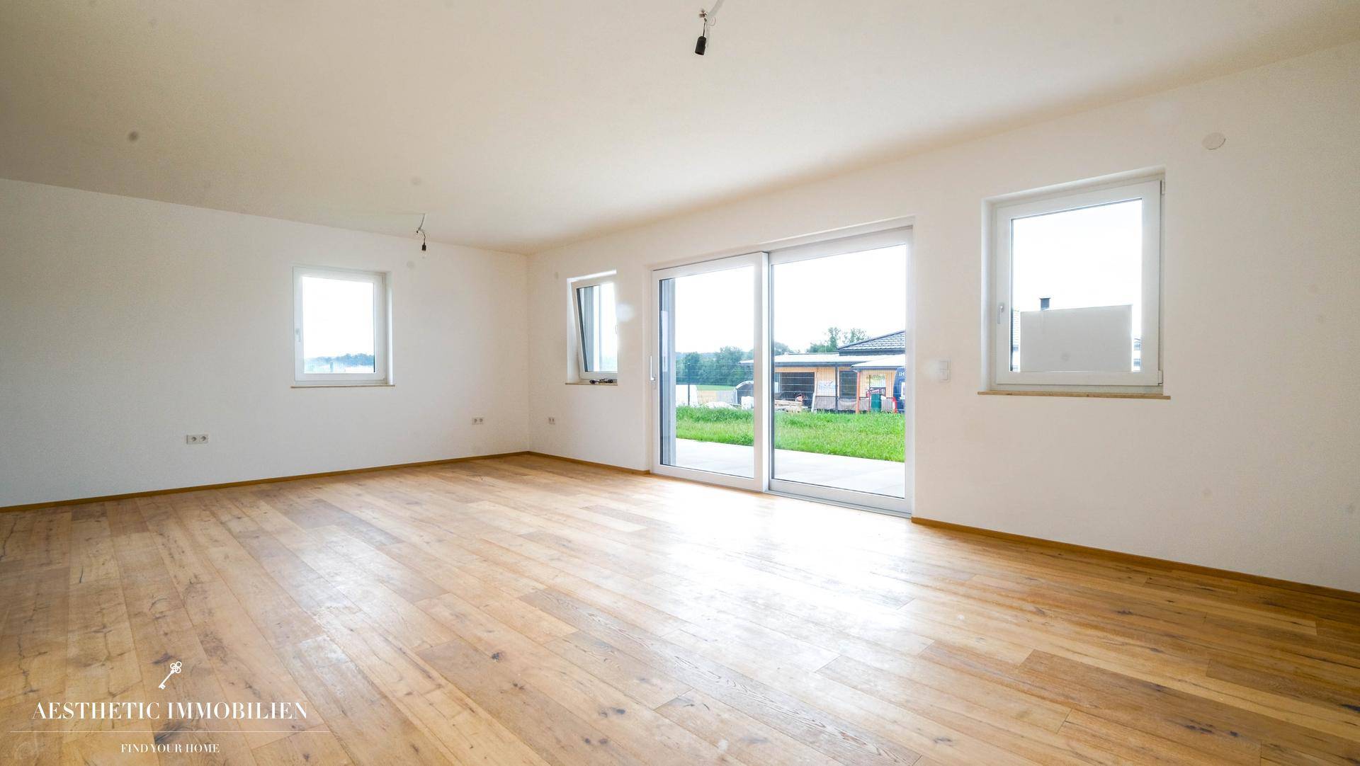 Geräumiges, leeres Wohnzimmer mit Holzboden und Zugang zur Terrasse durch große Schiebetüren.