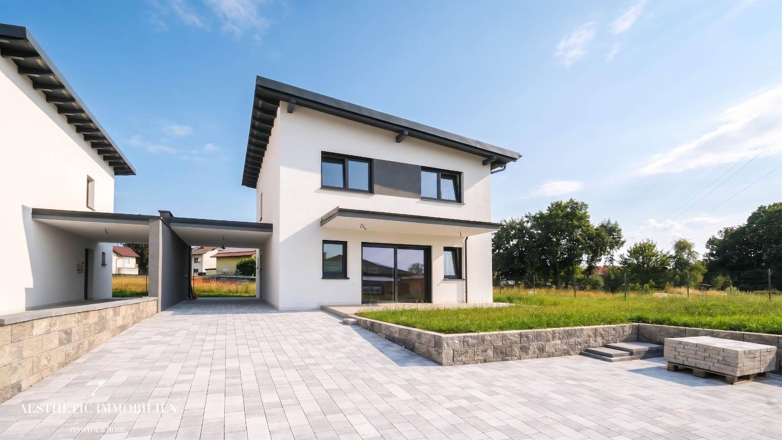 Moderne Doppelhaushälfte mit klaren Linien, Carport und gepflasterter Einfahrt unter blauem Himmel.