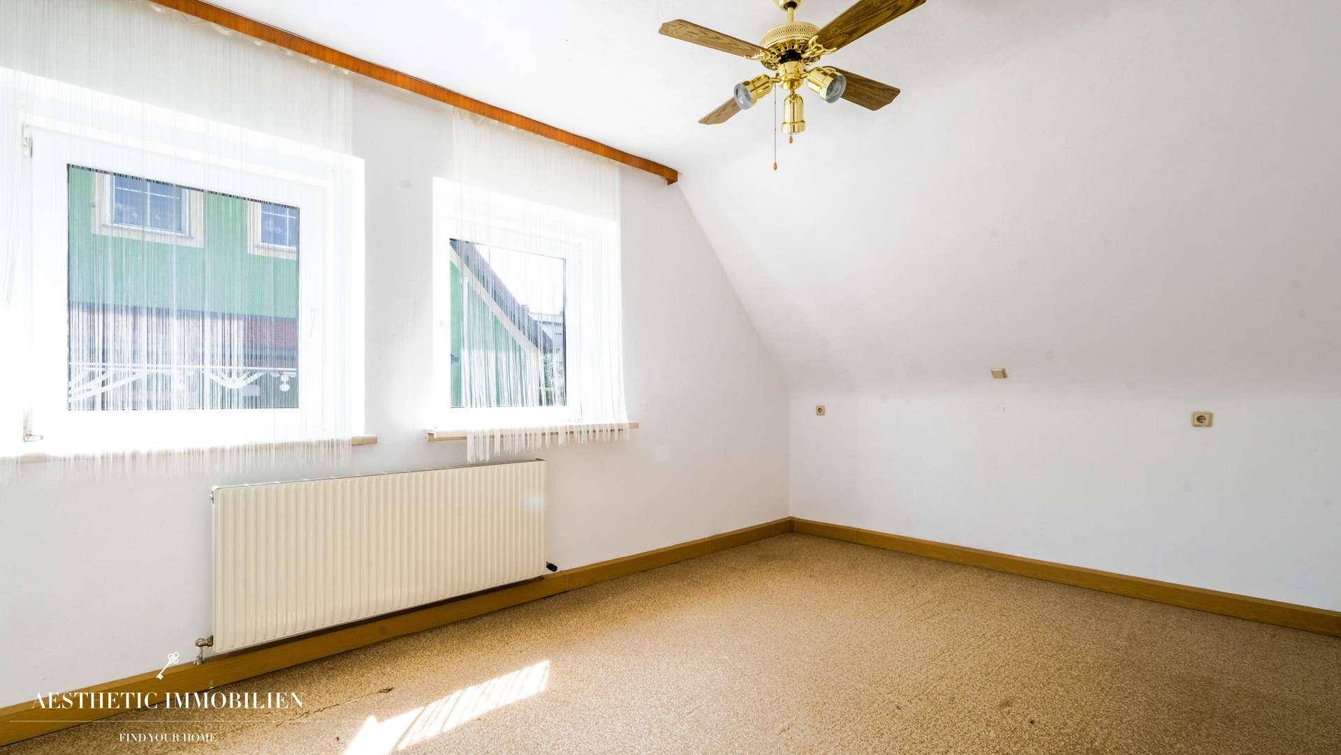 Helles Schlafzimmer im Dachgeschoss mit Teppichboden und Deckenventilator.