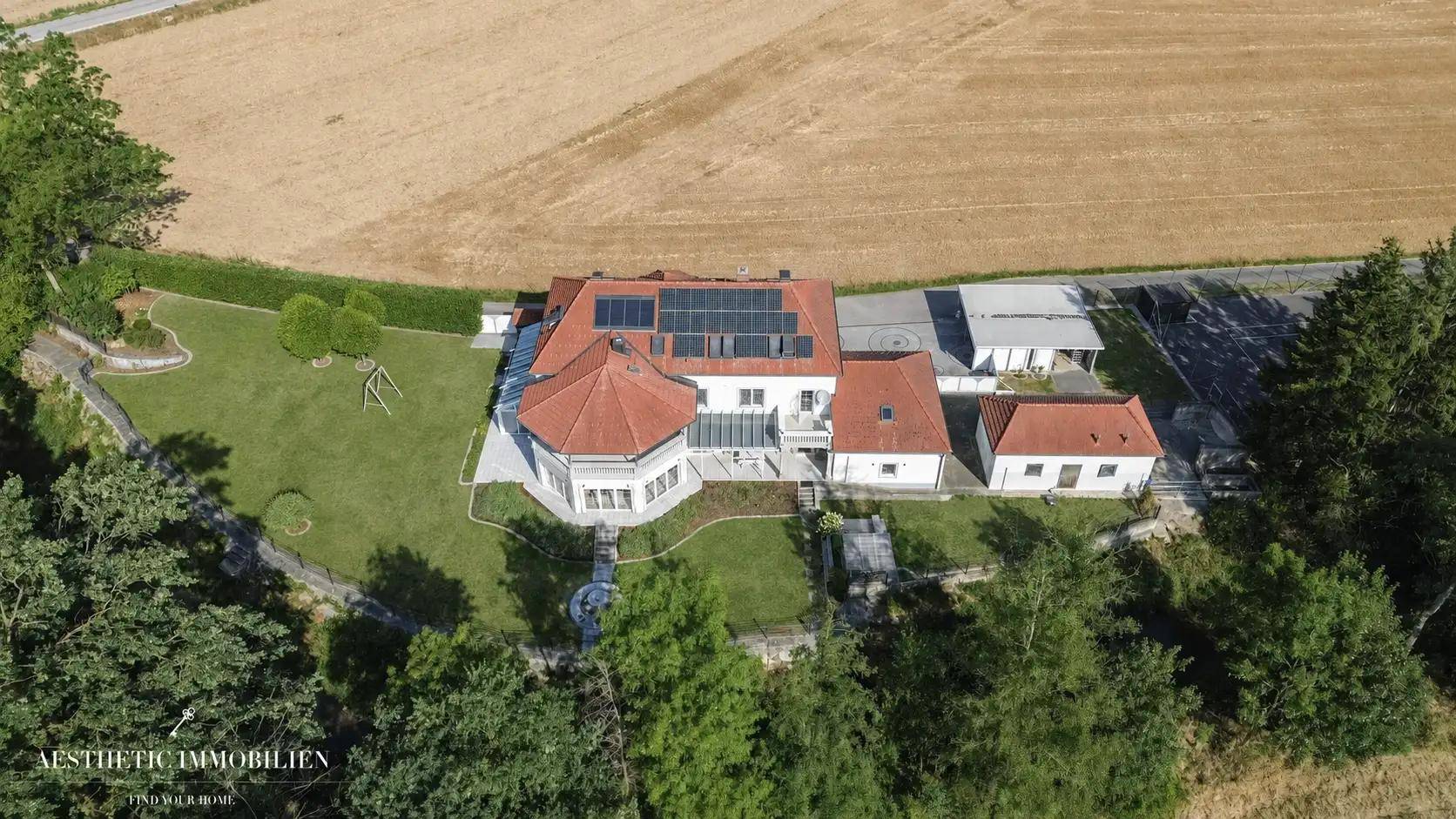 Gesamtansicht des Anwesens aus der Luft mit Hauptgebäude, Nebengebäuden und Sportplatz.