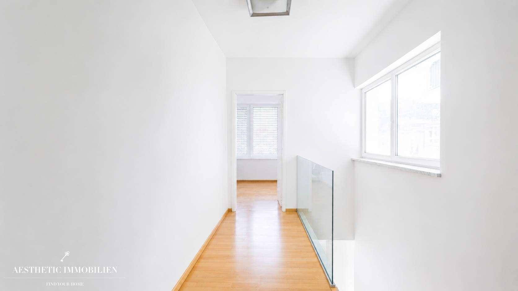 Heller Flur mit Holzboden, weißen Wänden und modernem Glasgeländer, das den Blick nach unten freigibt.