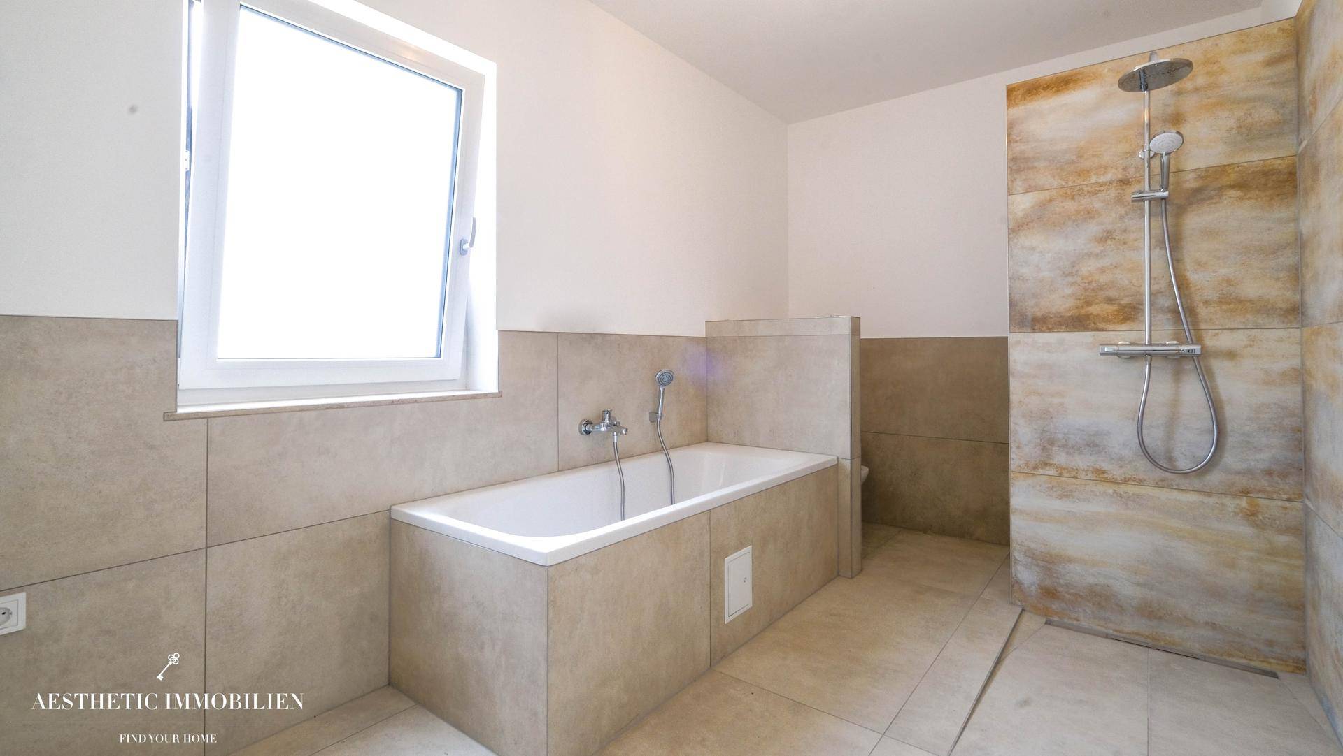 Modernes Badezimmer mit Badewanne, ebenerdiger Dusche, Fenster und hellen Fliesen.