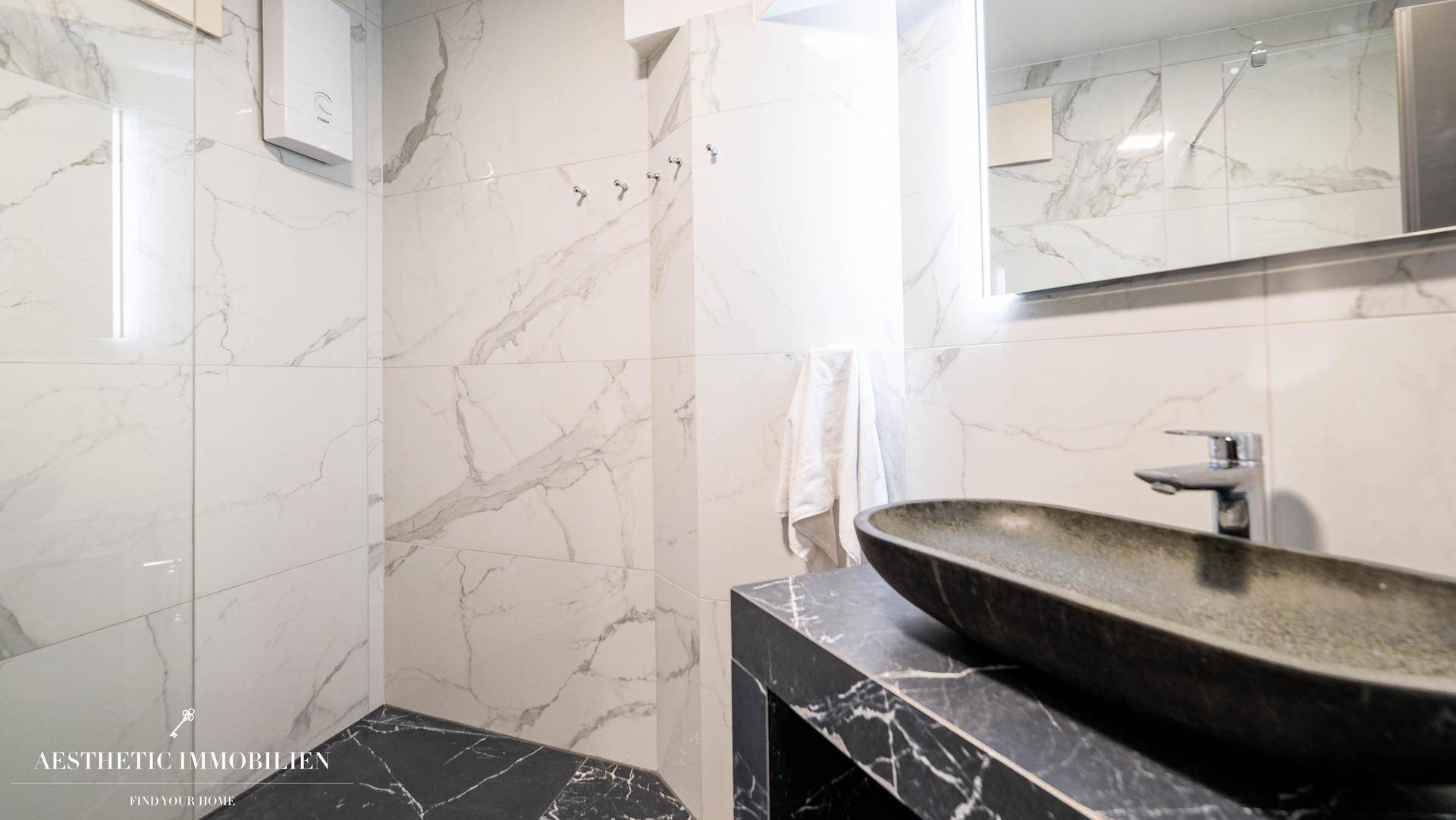 Modernes Badezimmer mit Marmorfliesen, schwarzem Waschbecken und begehbarer Dusche.