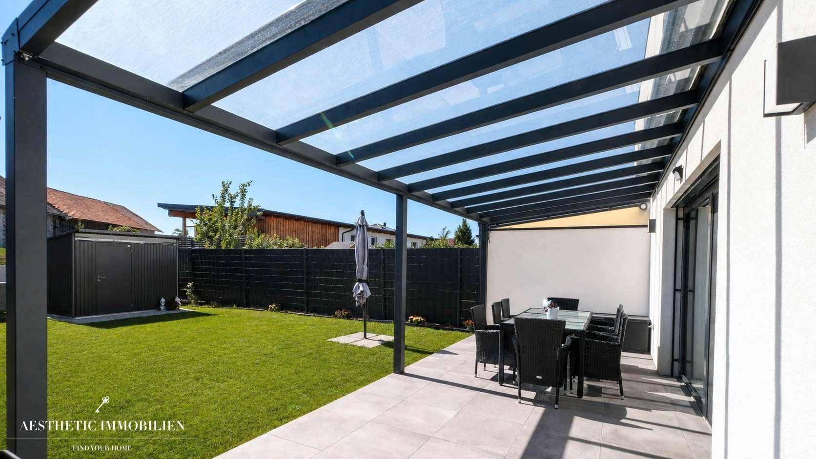 Überdachte Terrasse mit Gartenmöbeln und Blick auf den gepflegten Rasen und Gartenhaus.