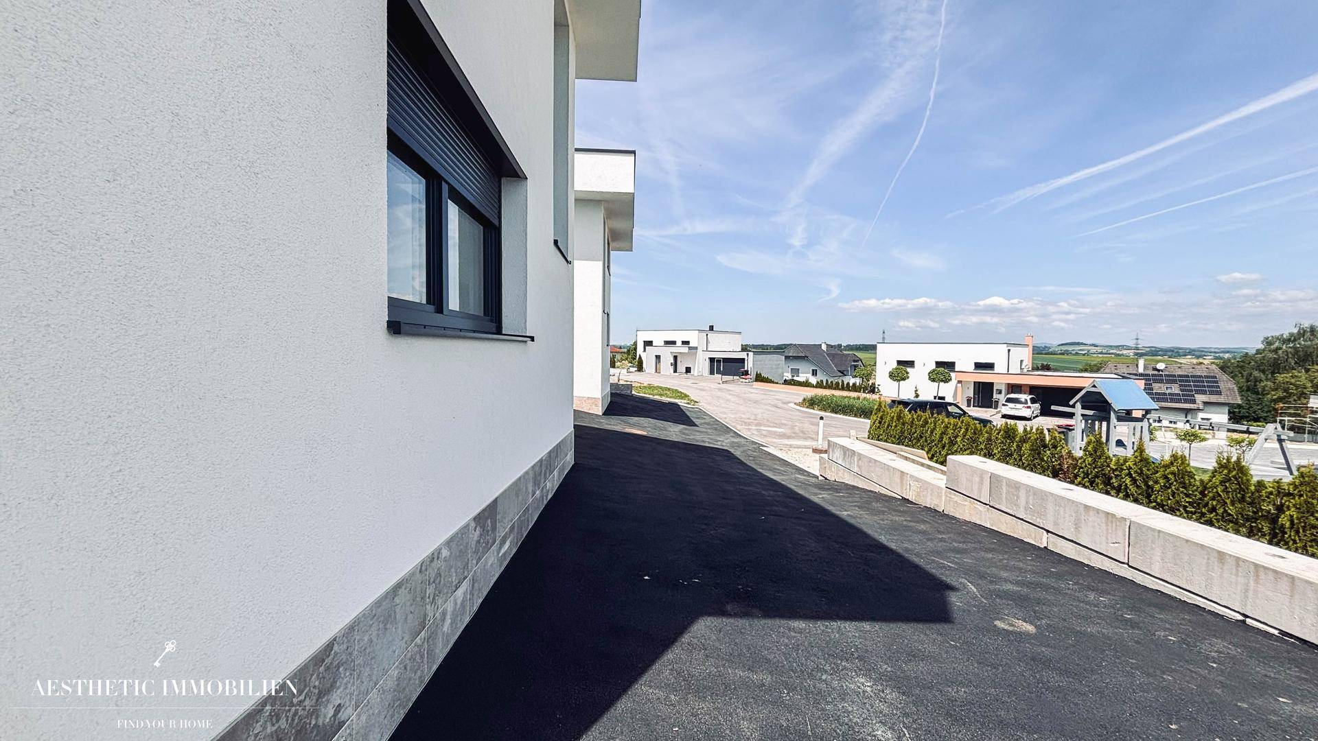 Seitenansicht eines modernen Hauses mit Zufahrt und Blick auf die Umgebung.