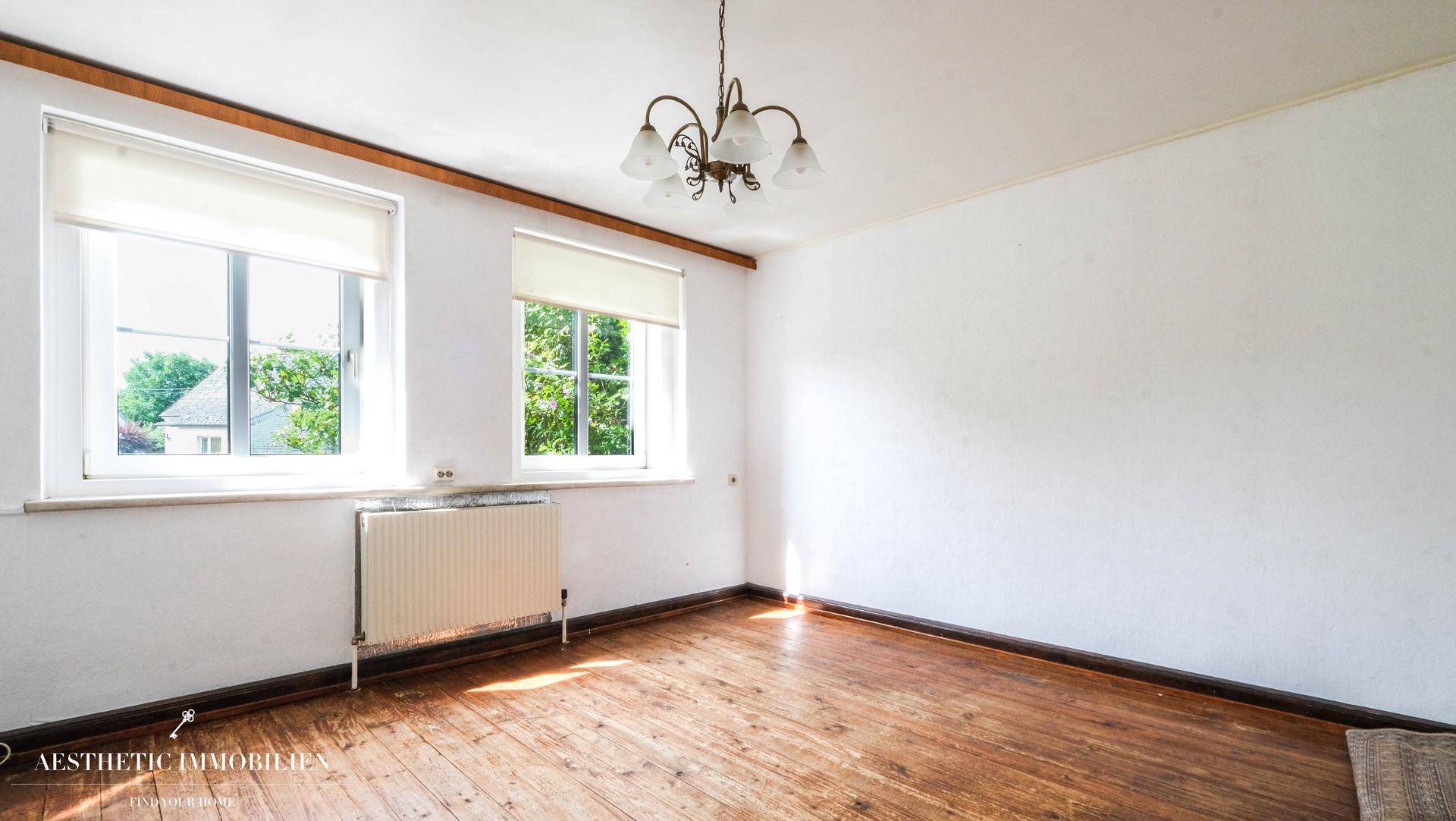 Heller Raum mit Holzdielenboden und zwei Fenstern, bereit zur individuellen Gestaltung.
