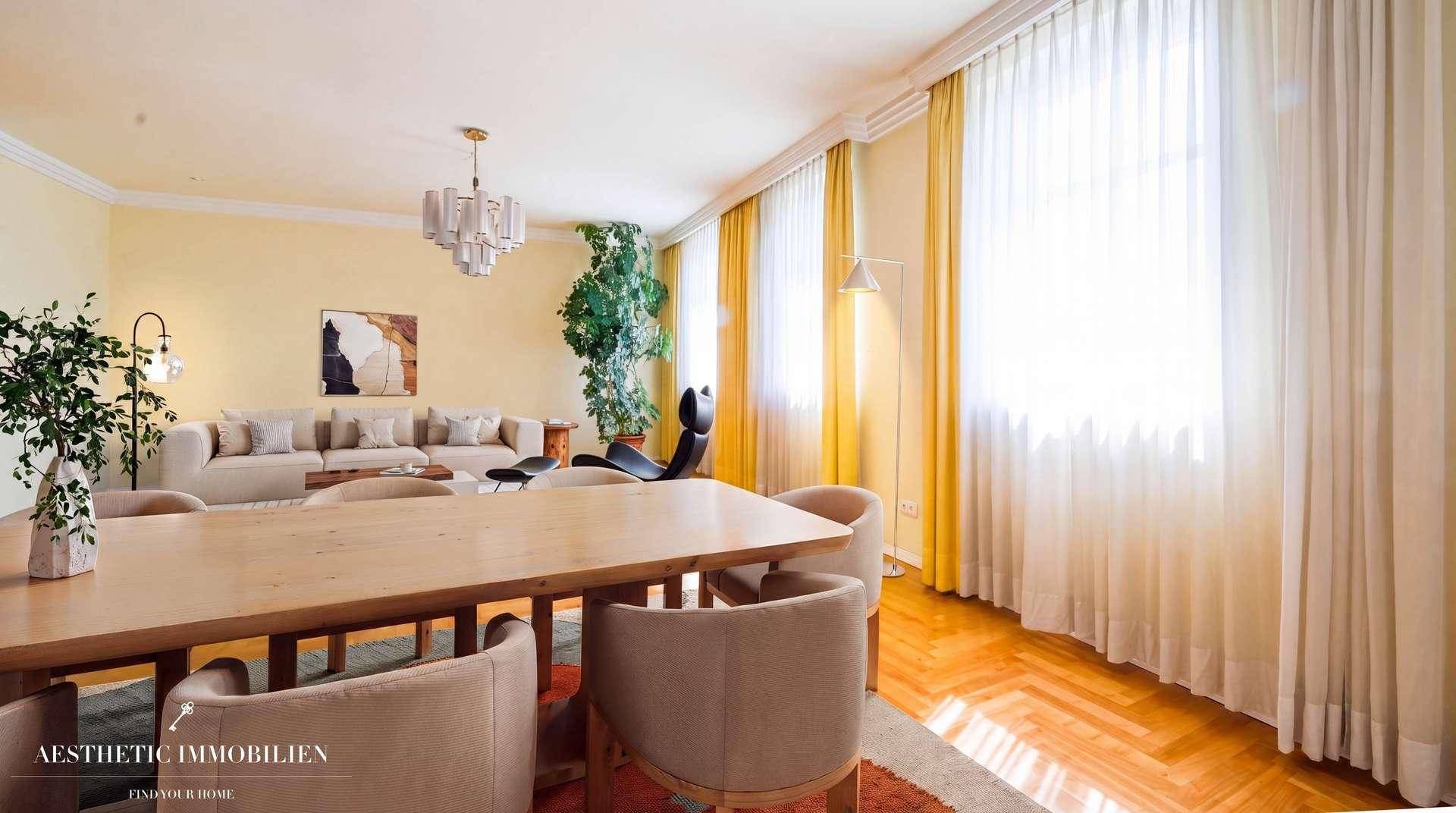 Heller Wohn- und Essbereich mit Parkettboden, großen Fenstern und eleganten Vorhängen.