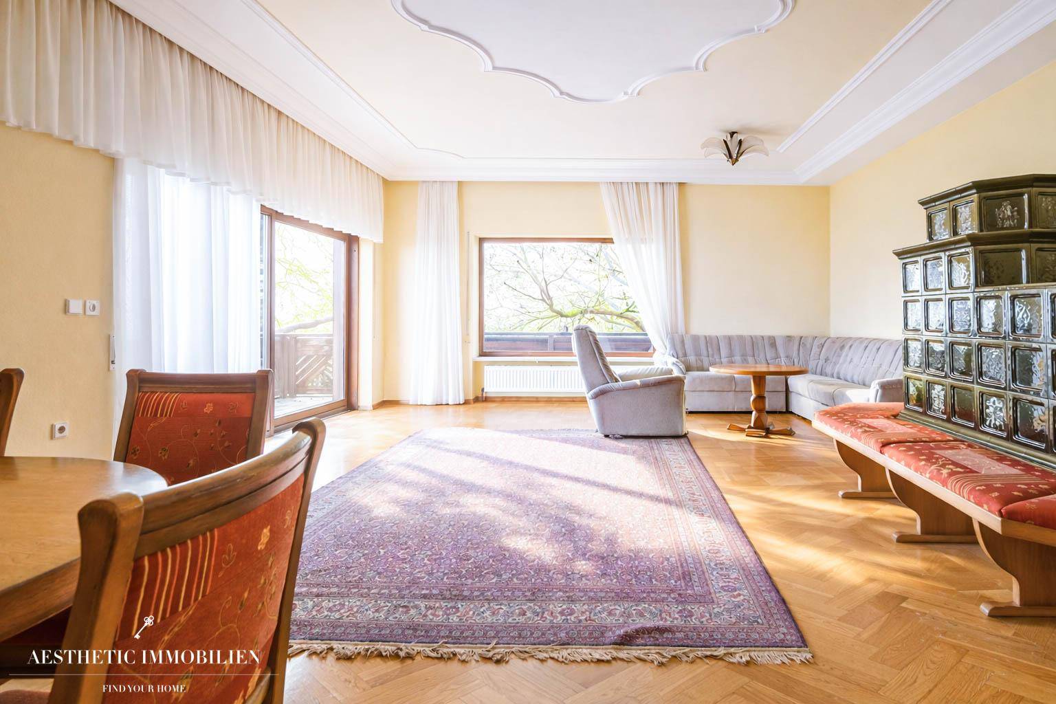 Geräumiger Wohnbereich mit traditionellem Kachelofen, Parkettboden und Zugang zum Balkon.