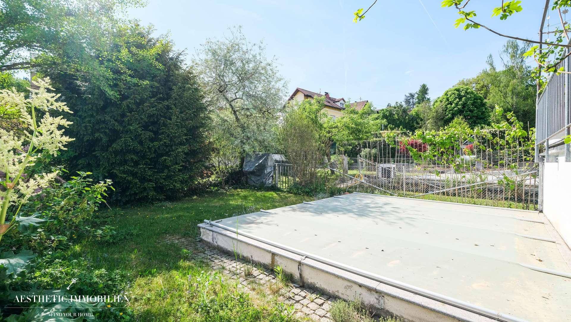 Grüner Gartenbereich mit einer abgedeckten Poolanlage, umgeben von Bäumen und Sträuchern.