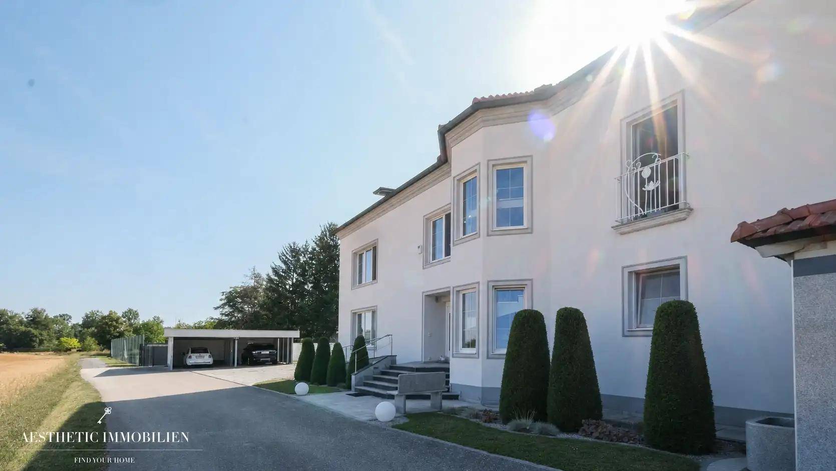 Sonnige Fassade des Hauses mit gepflegtem Vorgarten und Carport im Hintergrund.