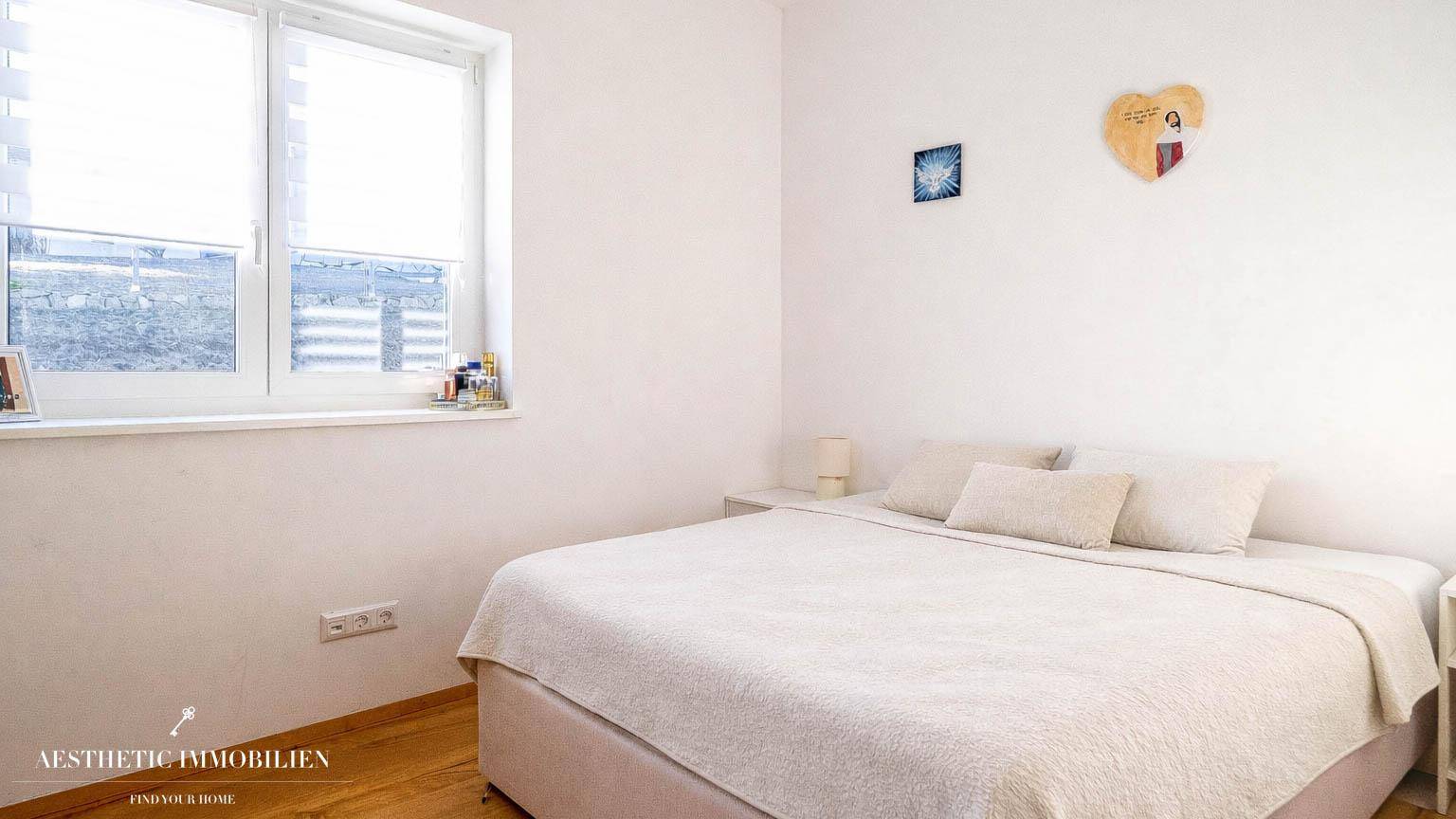 Helles Schlafzimmer mit Doppelbett, Holzboden und großem Fenster.