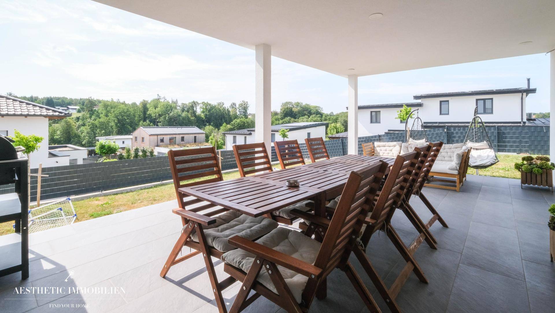 Geräumige überdachte Terrasse mit großem Esstisch und Blick ins Grüne.