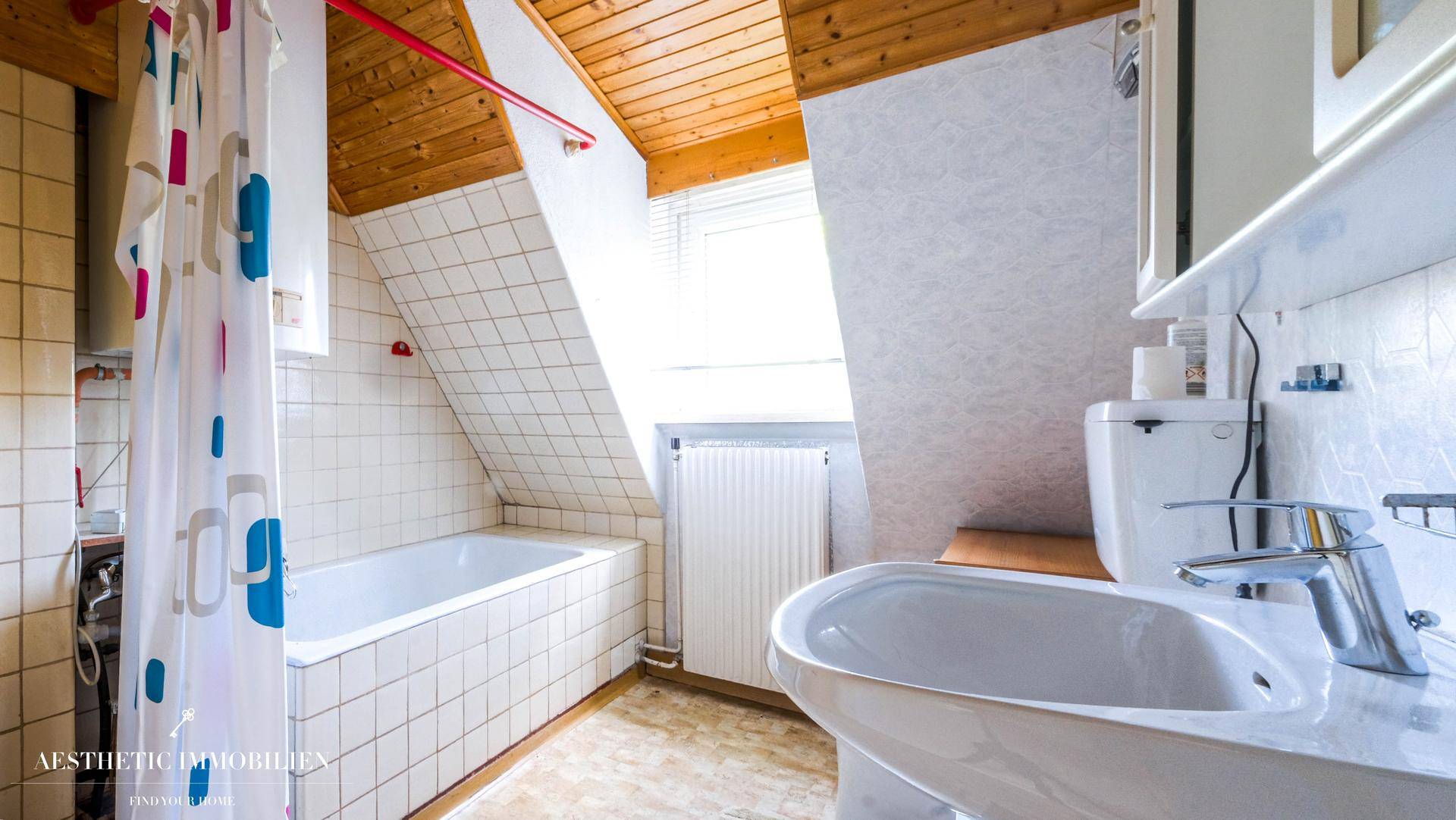 Helles Badezimmer im Dachgeschoss mit Badewanne, Waschbecken und Dachschräge.