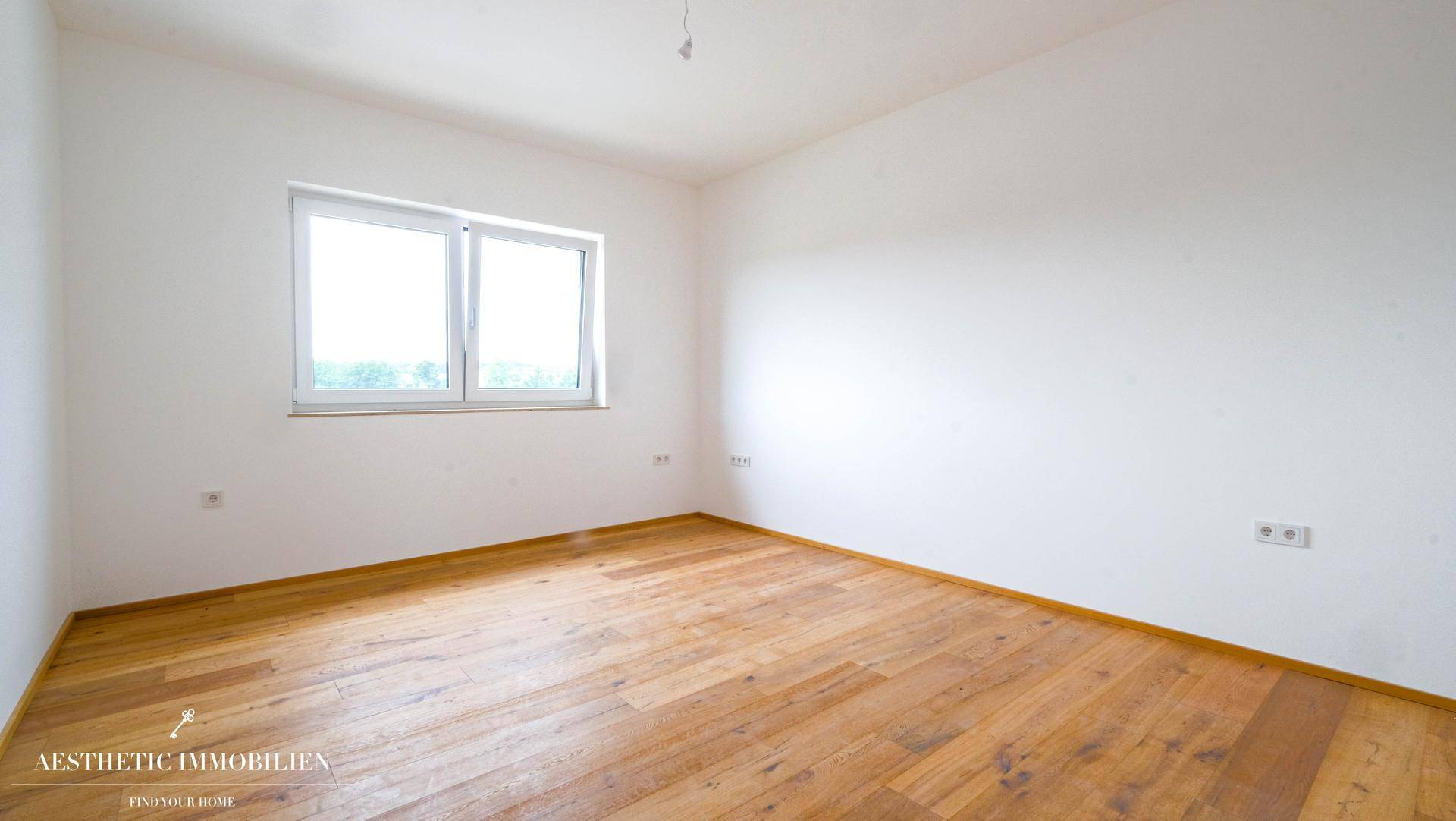 Leeres Zimmer mit Holzboden und einem großen Fenster, ideal als Schlaf- oder Arbeitszimmer.