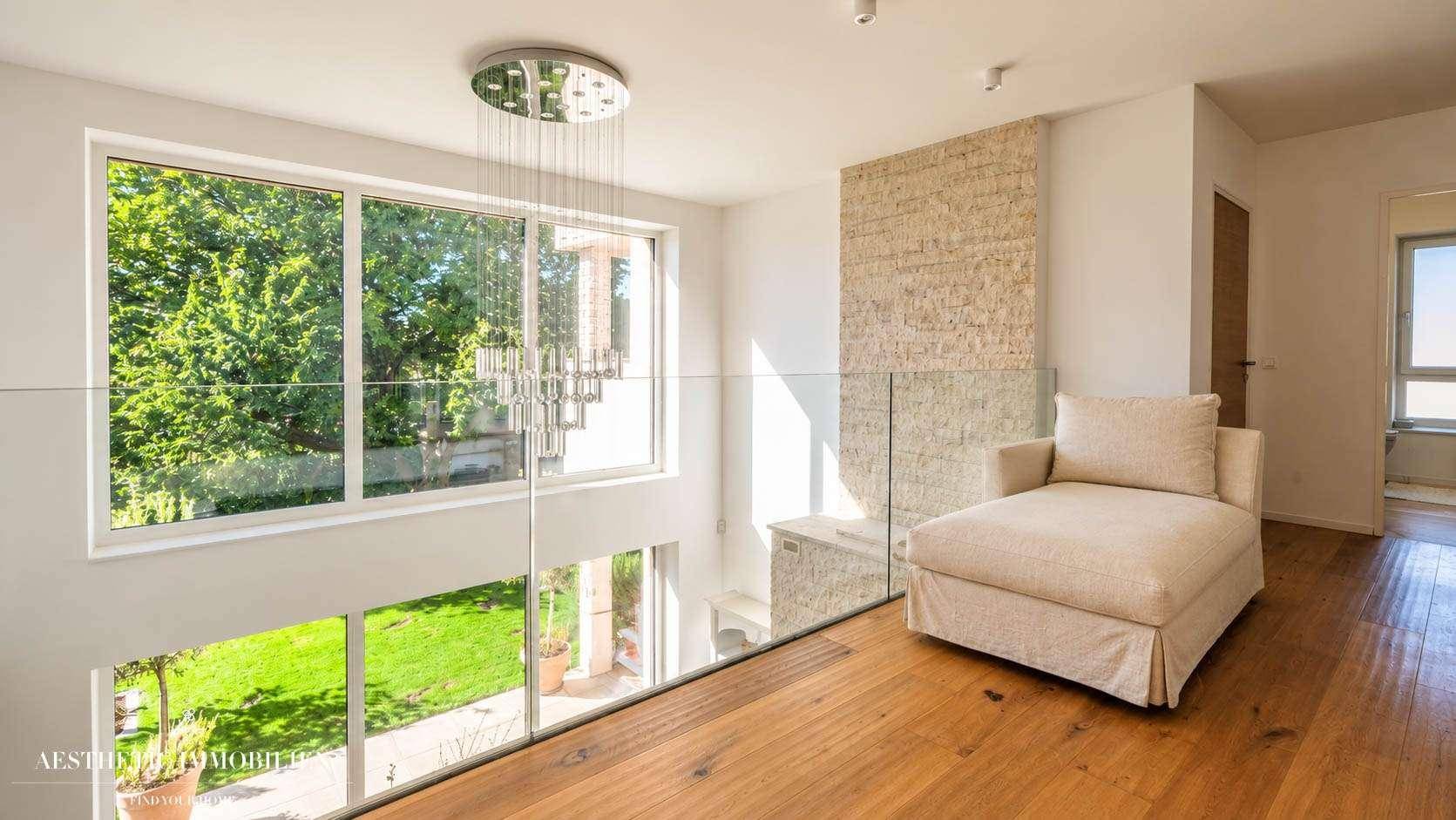 Helle Galerie mit Glasgeländer, bequemer Liege und Blick auf den Garten.