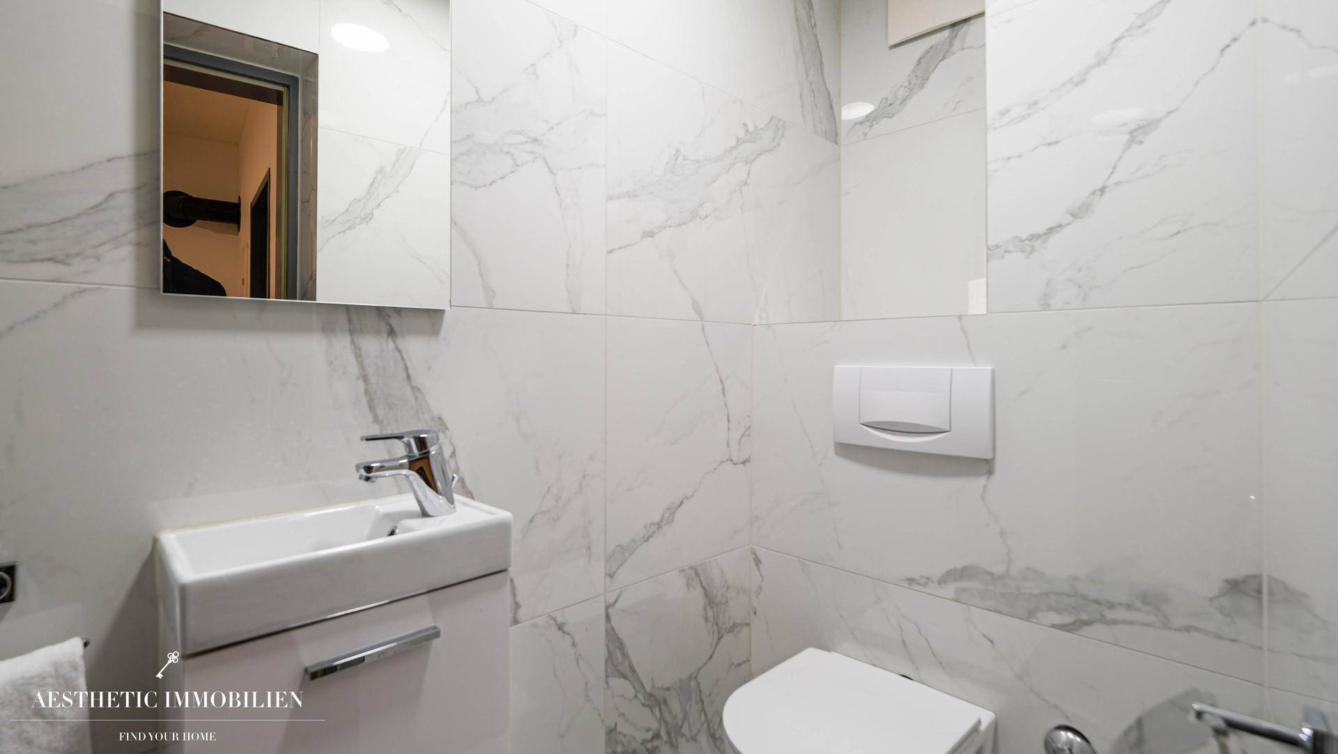 Modernes Gäste-WC mit Marmorfliesen, wandhängender Toilette und kleinem Waschbecken.