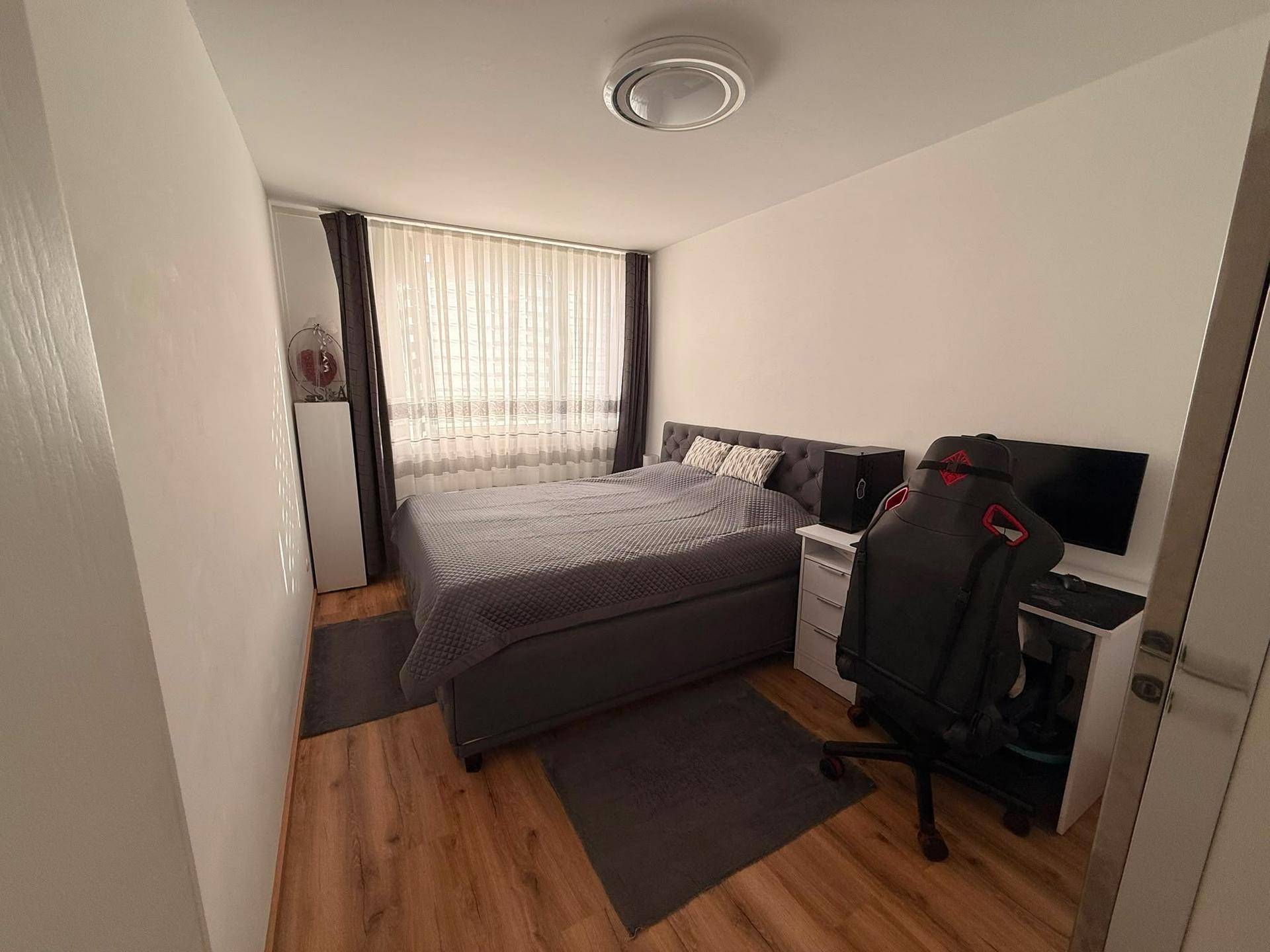 Schlafzimmer mit Doppelbett, Schreibtisch und Gaming-Stuhl, ideal für Home-Office.
