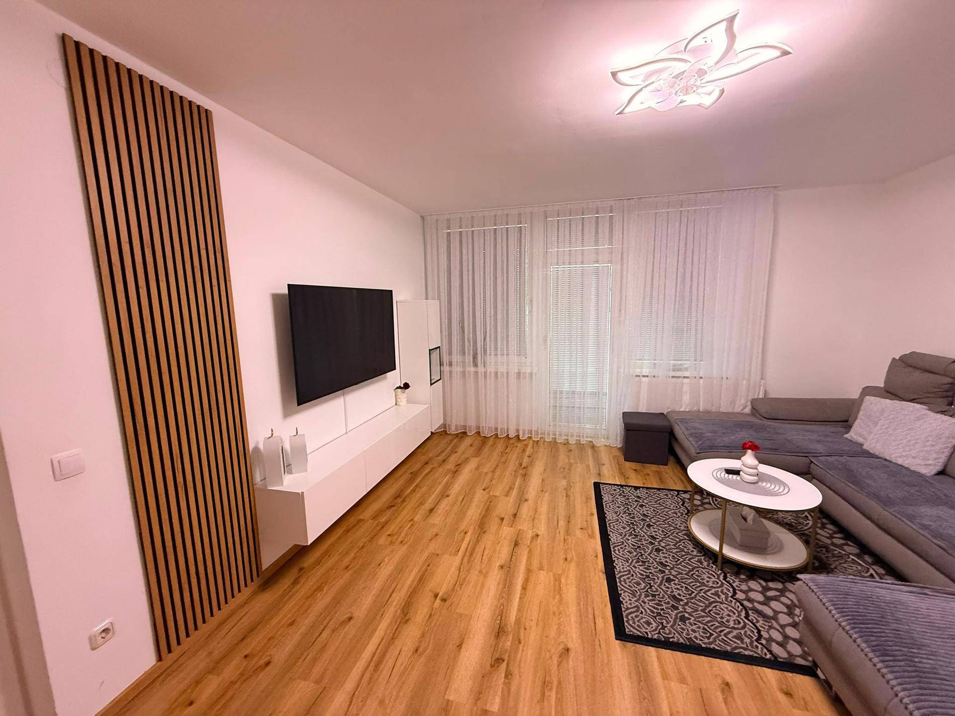 Gemütliches Wohnzimmer mit großem Sofa, Fernseher und dekorativer Holzlamellenwand.