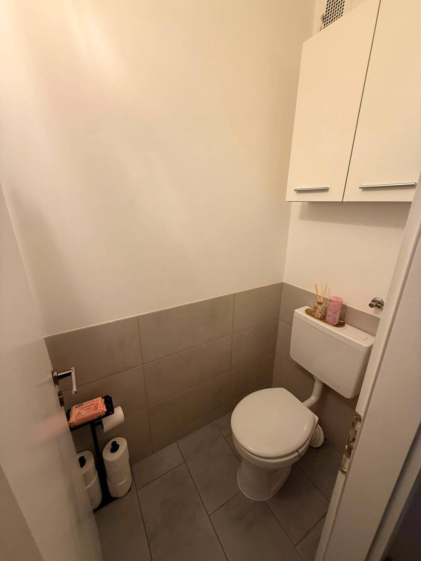 Kleines Gäste-WC mit Toilette, Wandfliesen und praktischem Hängeschrank.