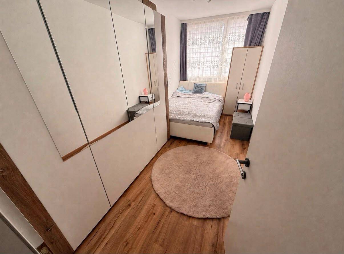 Schlafzimmer mit Doppelbett, Nachttischen und großem Spiegelschrank auf Holzfußboden.