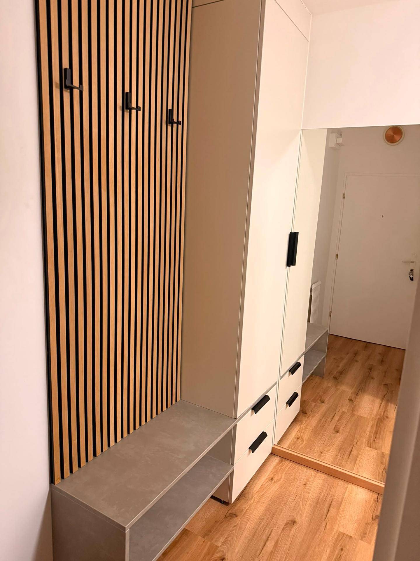 Eingangsbereich mit moderner Holzlamellenwand, Garderobe und integrierter Sitzbank.