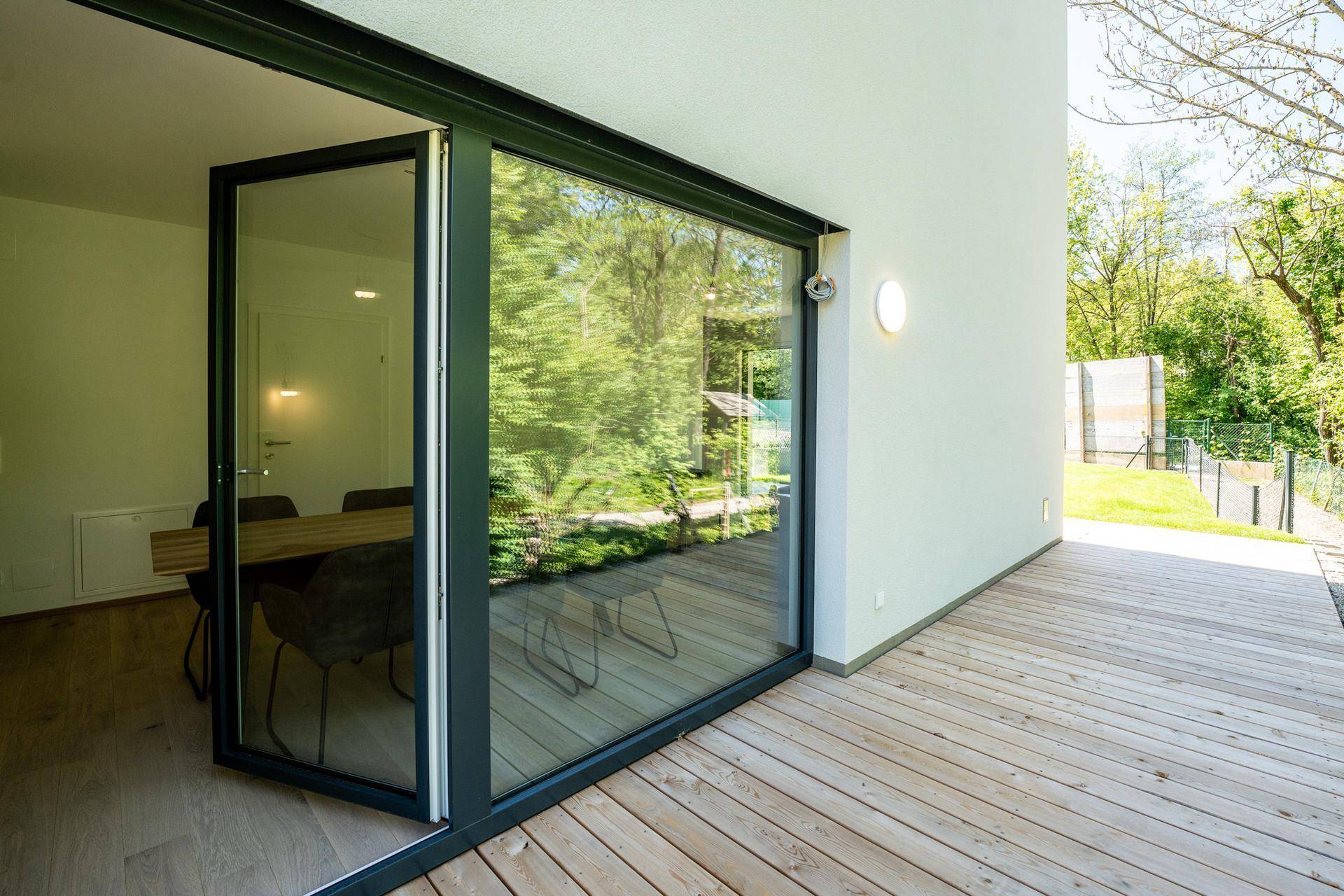 Helle Holzterrasse mit großzügiger Glasfront, die den Blick ins Grüne freigibt.
