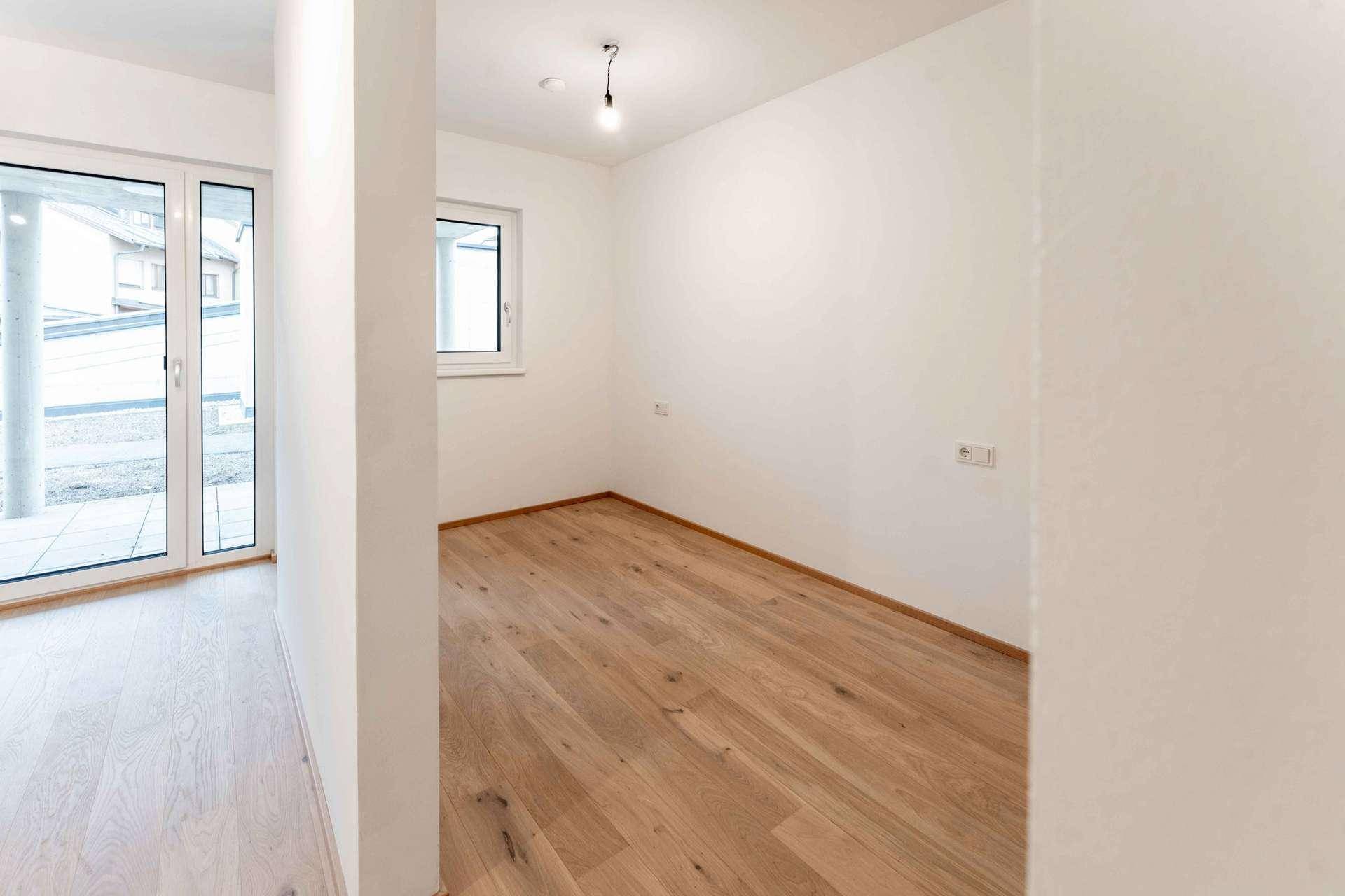 Helles Zimmer mit Holzboden und Fenster, bietet vielseitige Nutzungsmöglichkeiten im Neubau.