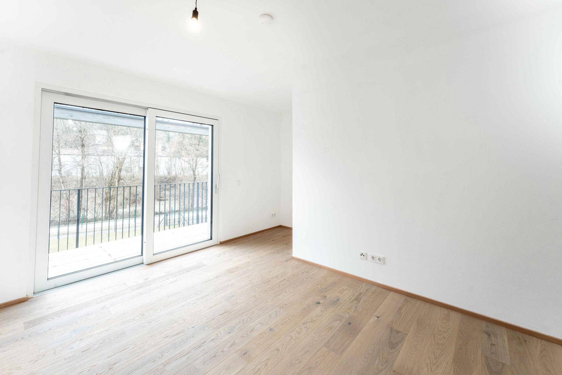 Helles Wohnzimmer mit Eichenparkett und Zugang zu einem Balkon.
