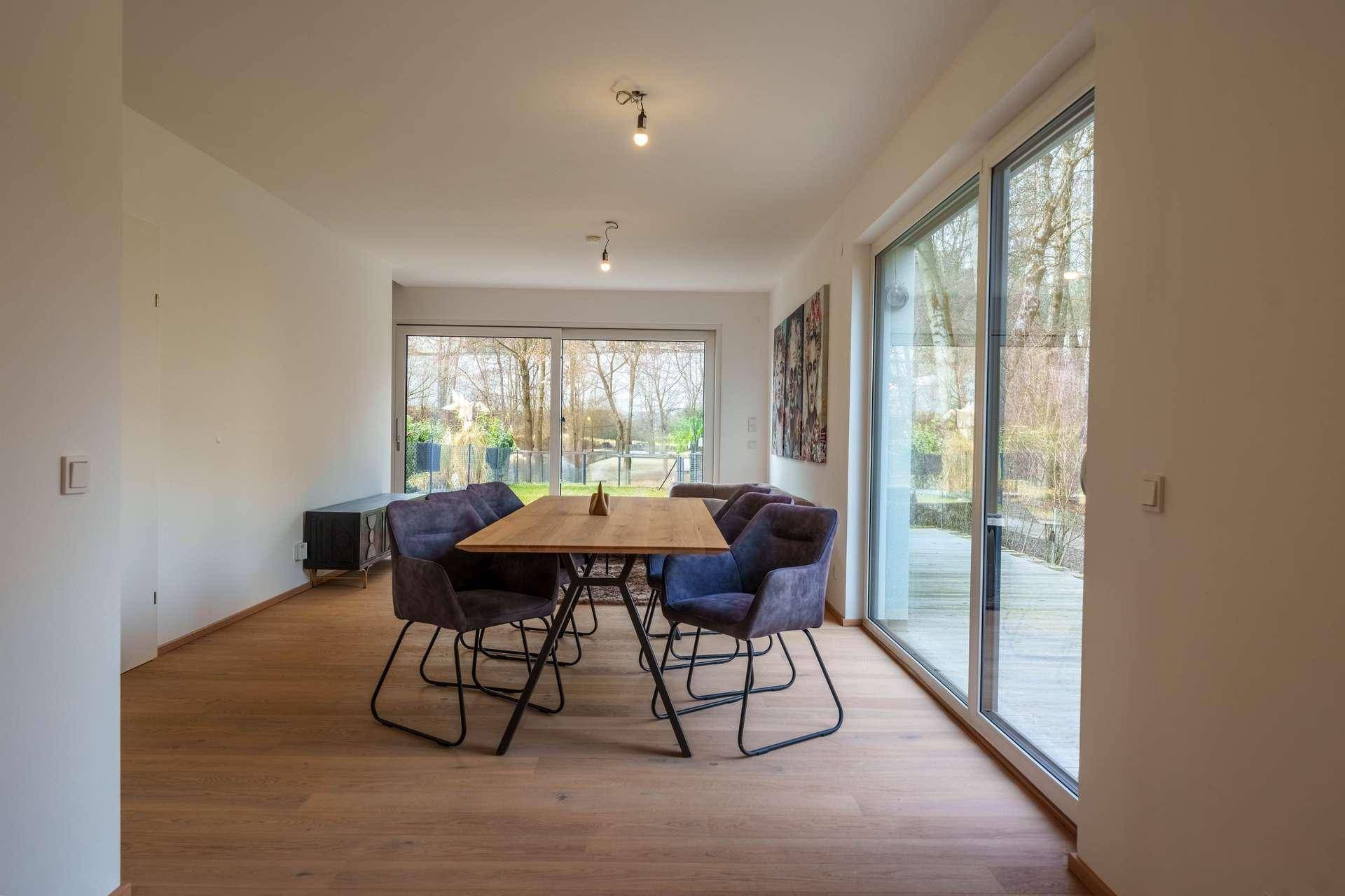 Lichtdurchfluteter Essbereich mit Holzboden und großen Fenstern, die den Garten zeigen.