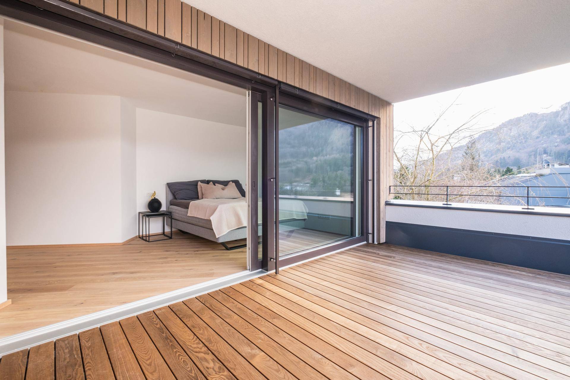 Geräumige Terrasse mit Holzboden und Zugang zu einem hellen Schlafzimmer mit Bergblick.