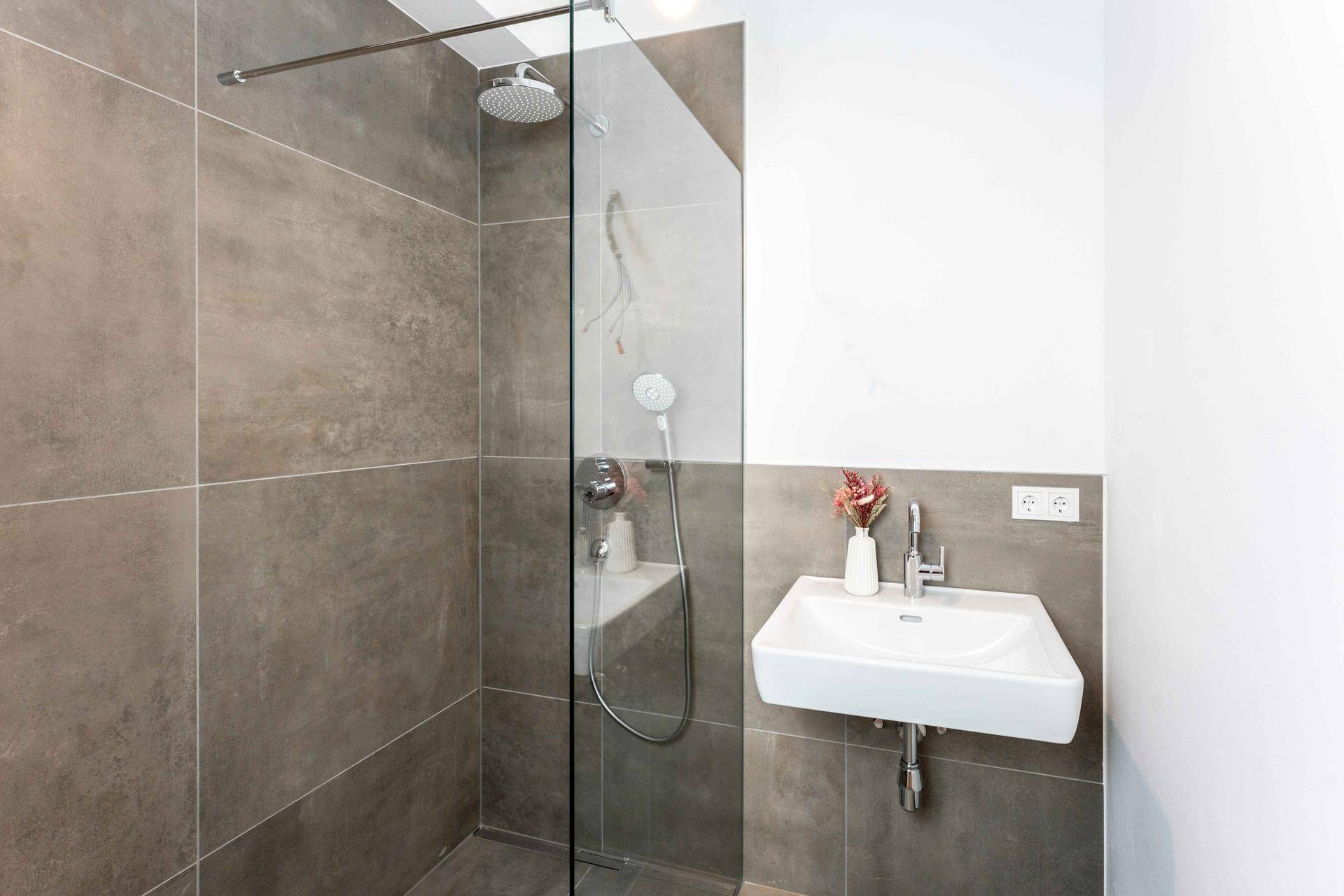 Moderne Dusche mit Glasabtrennung und Waschbecken in einem hellen Badezimmer.
