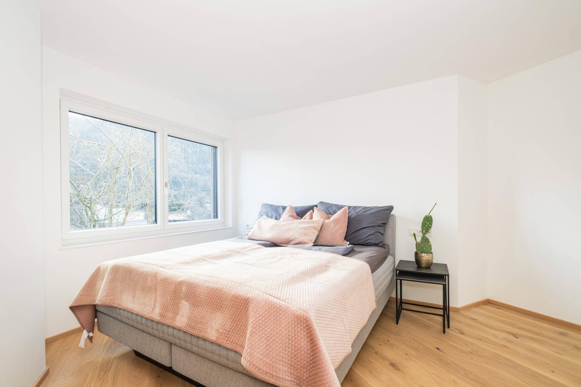 Helles Schlafzimmer mit Holzboden, großem Fenster und minimalistischer Einrichtung.