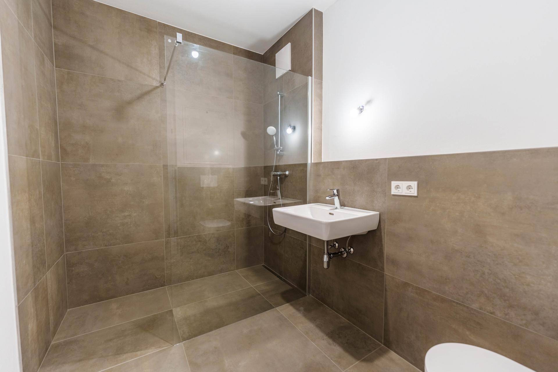 Modernes Badezimmer mit ebenerdiger Dusche, großen Wandfliesen und einem einzelnen Waschbecken.