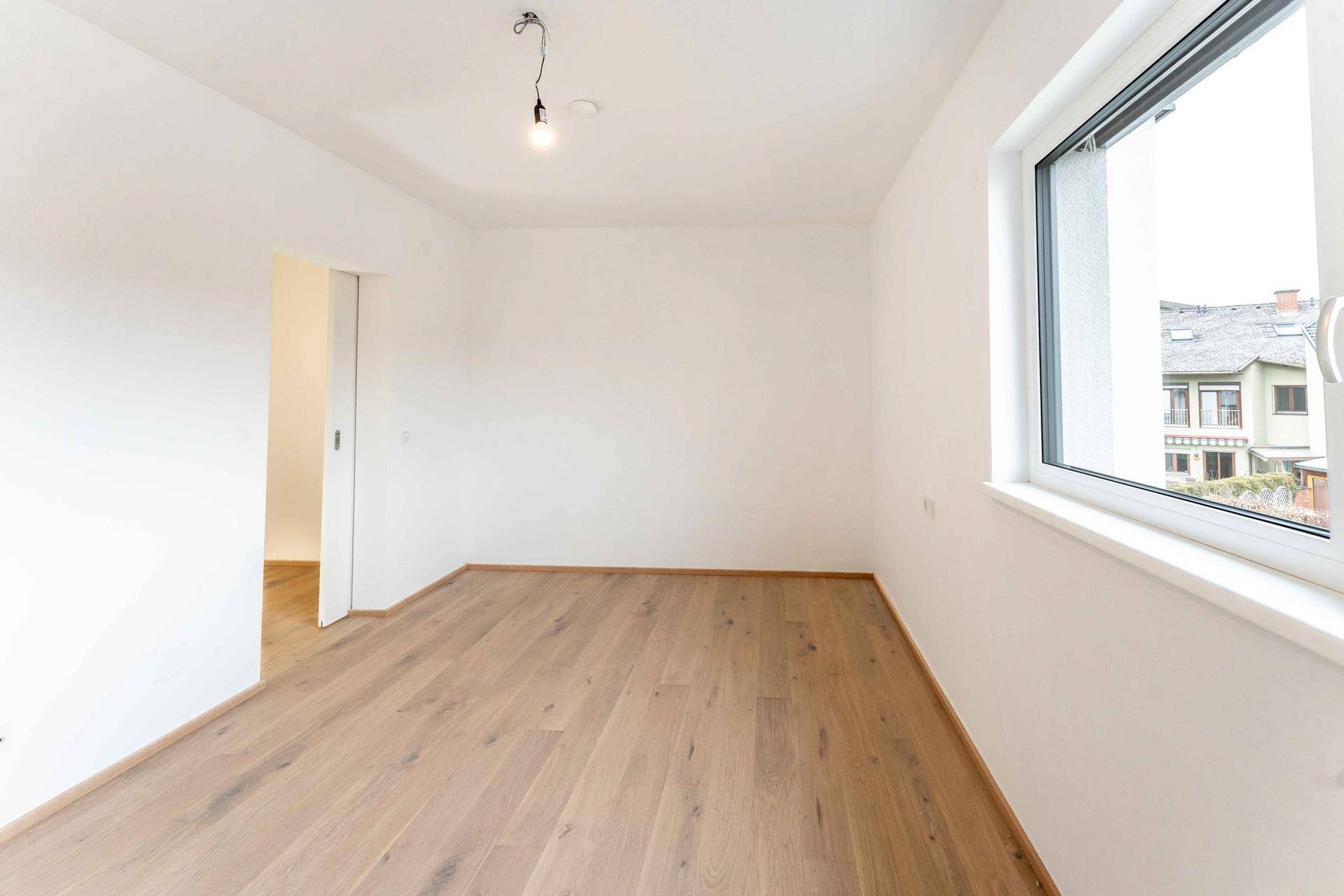 Geräumiges Zimmer mit hellem Parkettboden und großem Fenster.