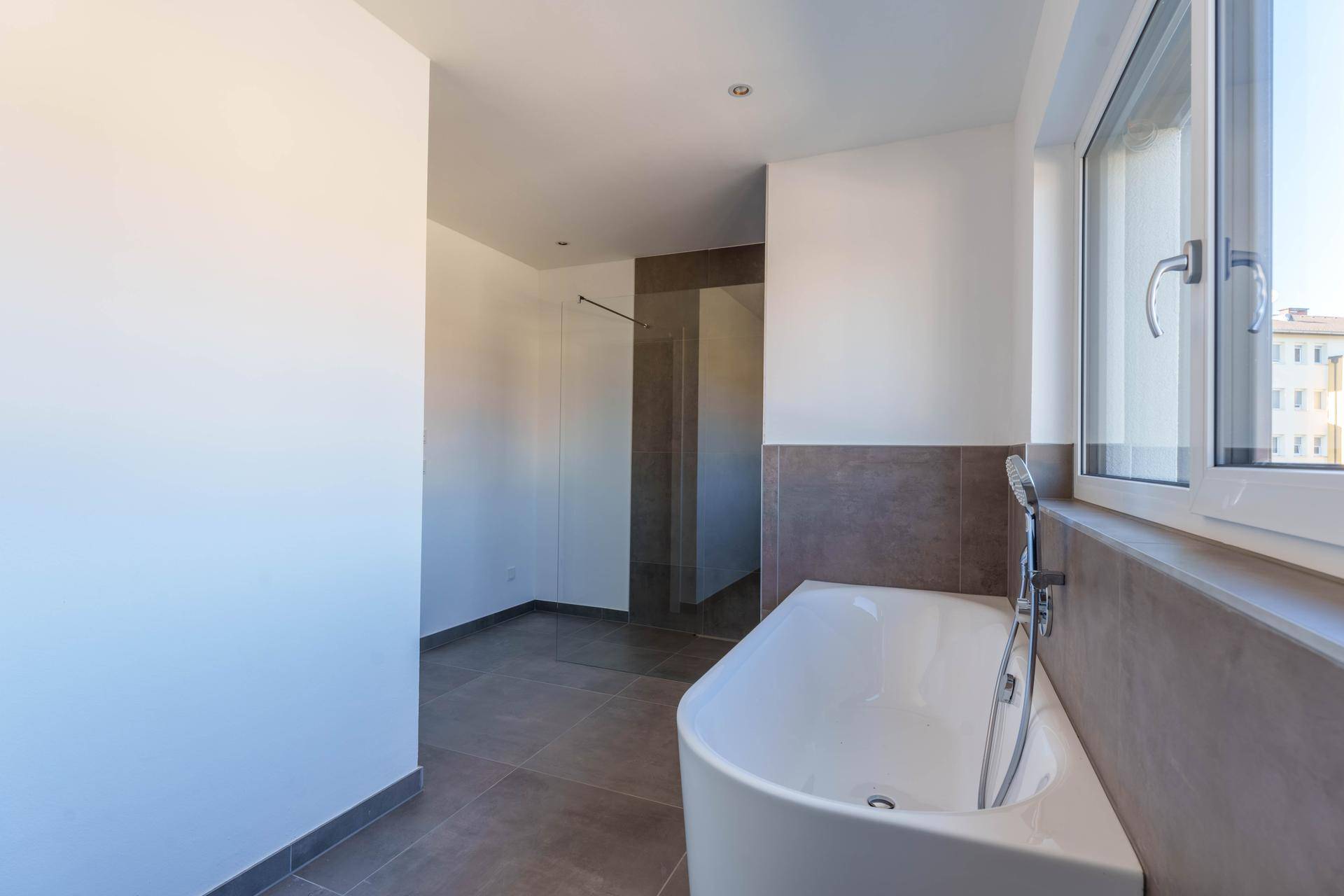Helles Badezimmer mit moderner Badewanne, großen Fliesen und einem Fenster für Tageslicht.